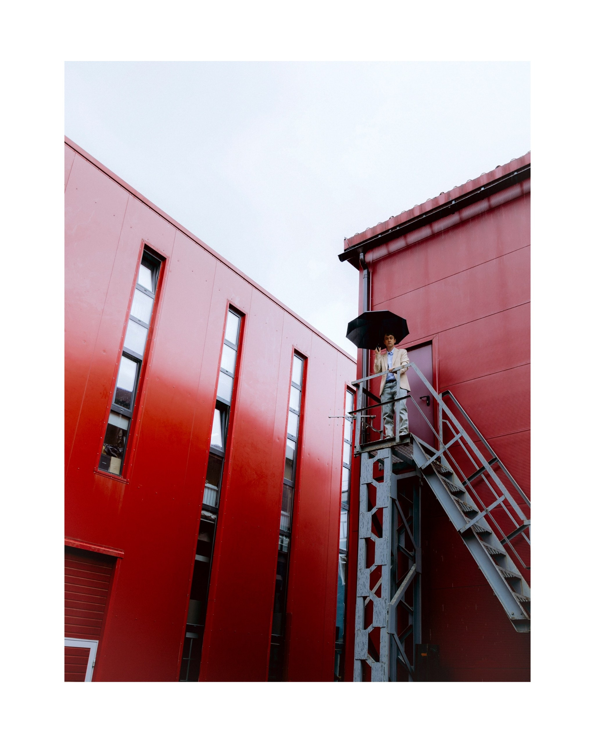 парень с зонтом на фоне красного здания 