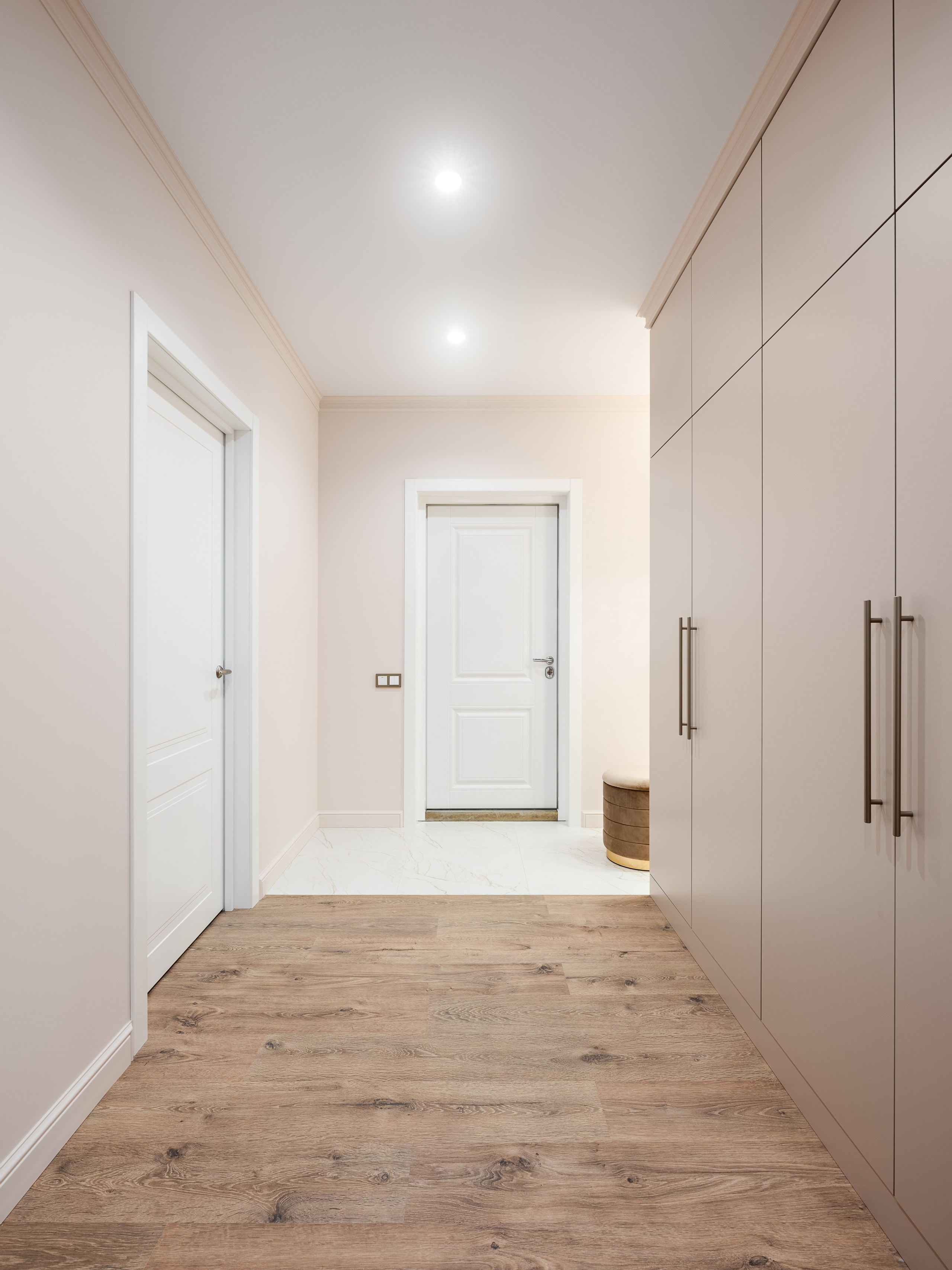 Просторная прихожая с встроенными шкафами в бежевых тонах, дверями с белыми филенками и тёплым деревянным полом, гармонирующим с минималистичным стилем. Дизайнер Наталья Бунеева, стилист Наталья Якушева, фотограф Сергей Денисенко.