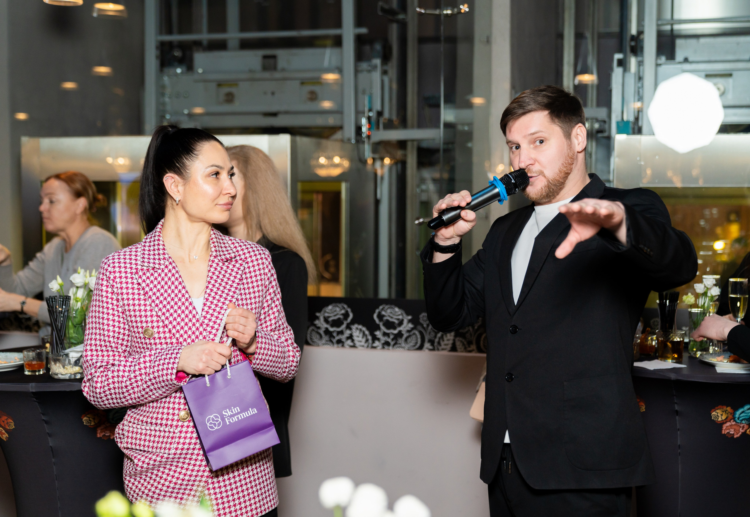Ведущий с микрофоном и женщина в розово-бордовом жакете на мероприятии. Фото Евгения Мальцева, Radisson Sonya Hotel St. Petersburg.