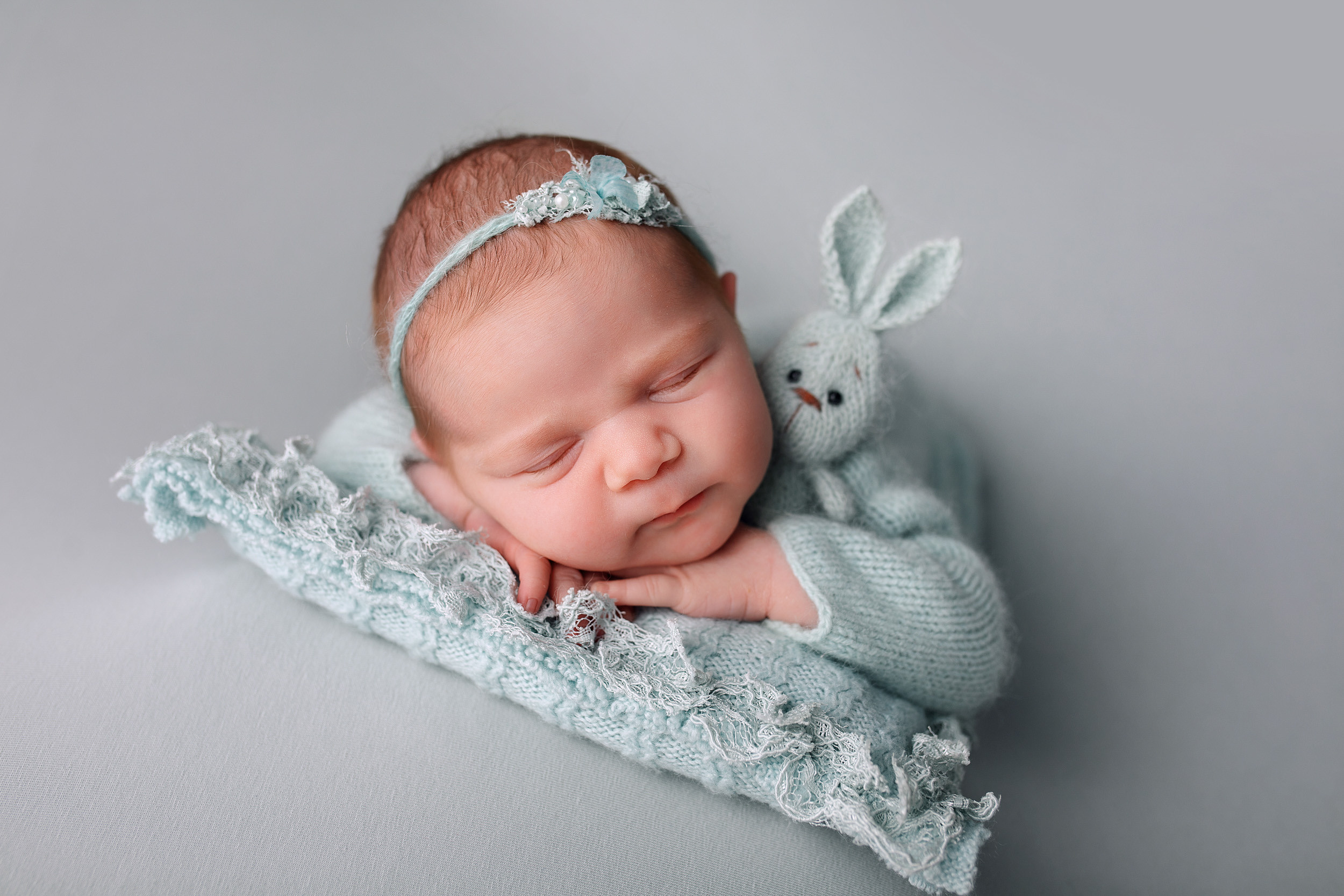 новорожденная девочка на фотосессии лежит на подушечке ручки под подбородком