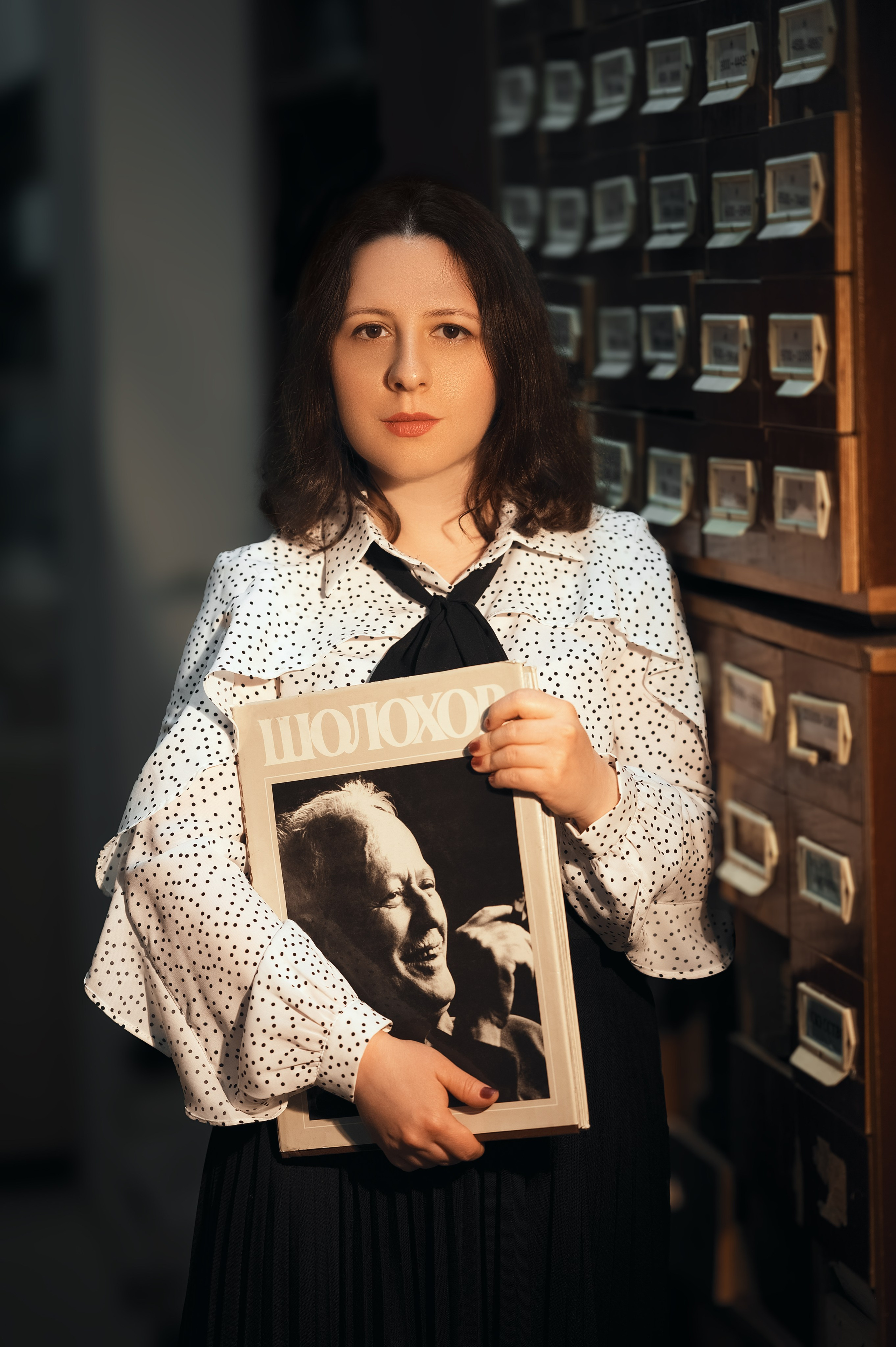 Портретная съёмка в Волгодонске: девушка среди книжных стеллажей. Светлая блузка и тёмная юбка, книга в руках. Работа фотографа Елизаветы Жуйковой.