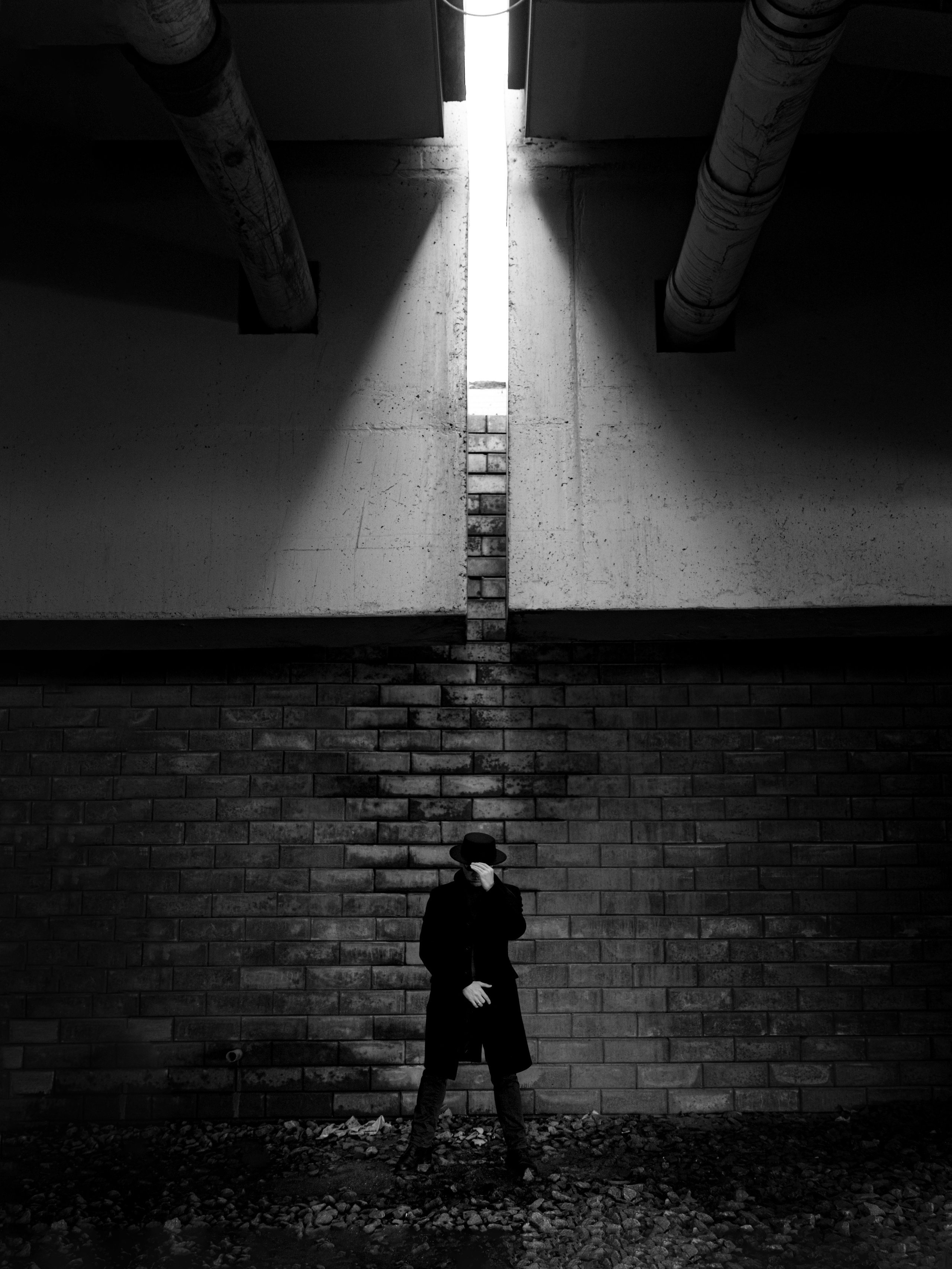 Творческая черно-белая фотография мужчины в пальто у кирпичной стены