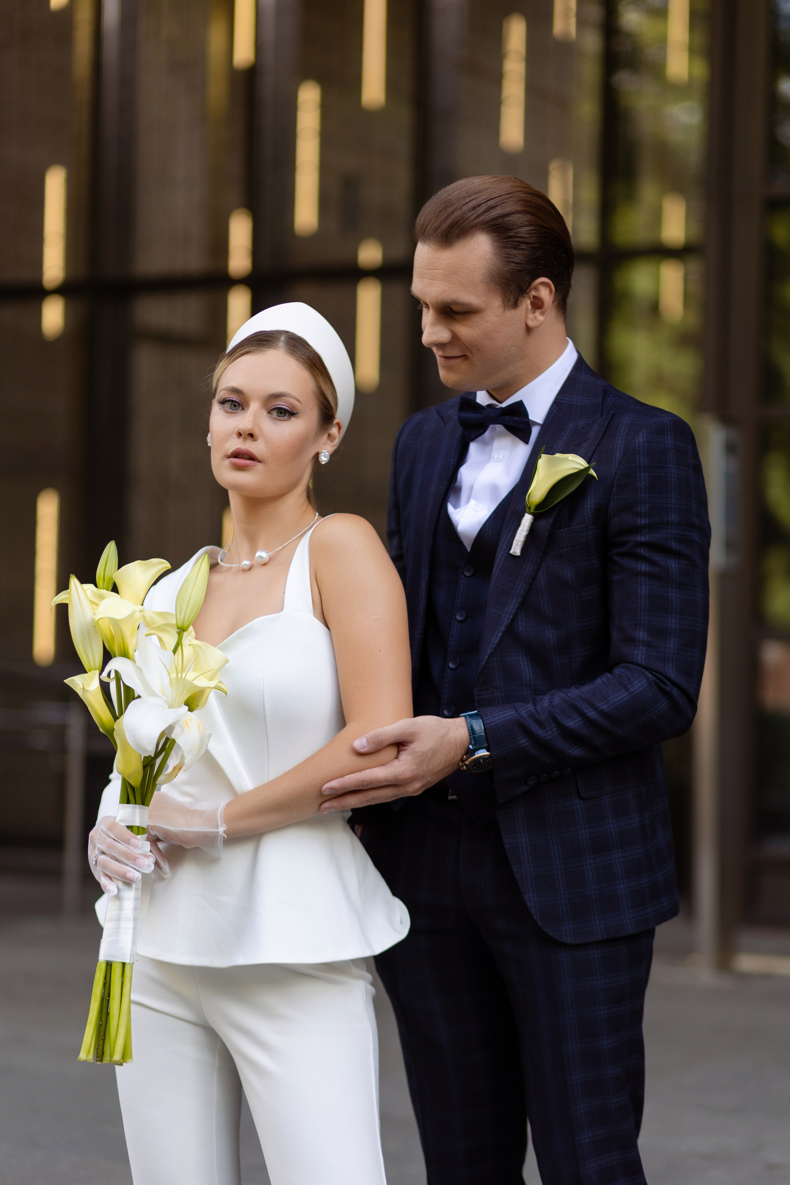 Невеста стоит держа в руках букет. сзади стоит жених.