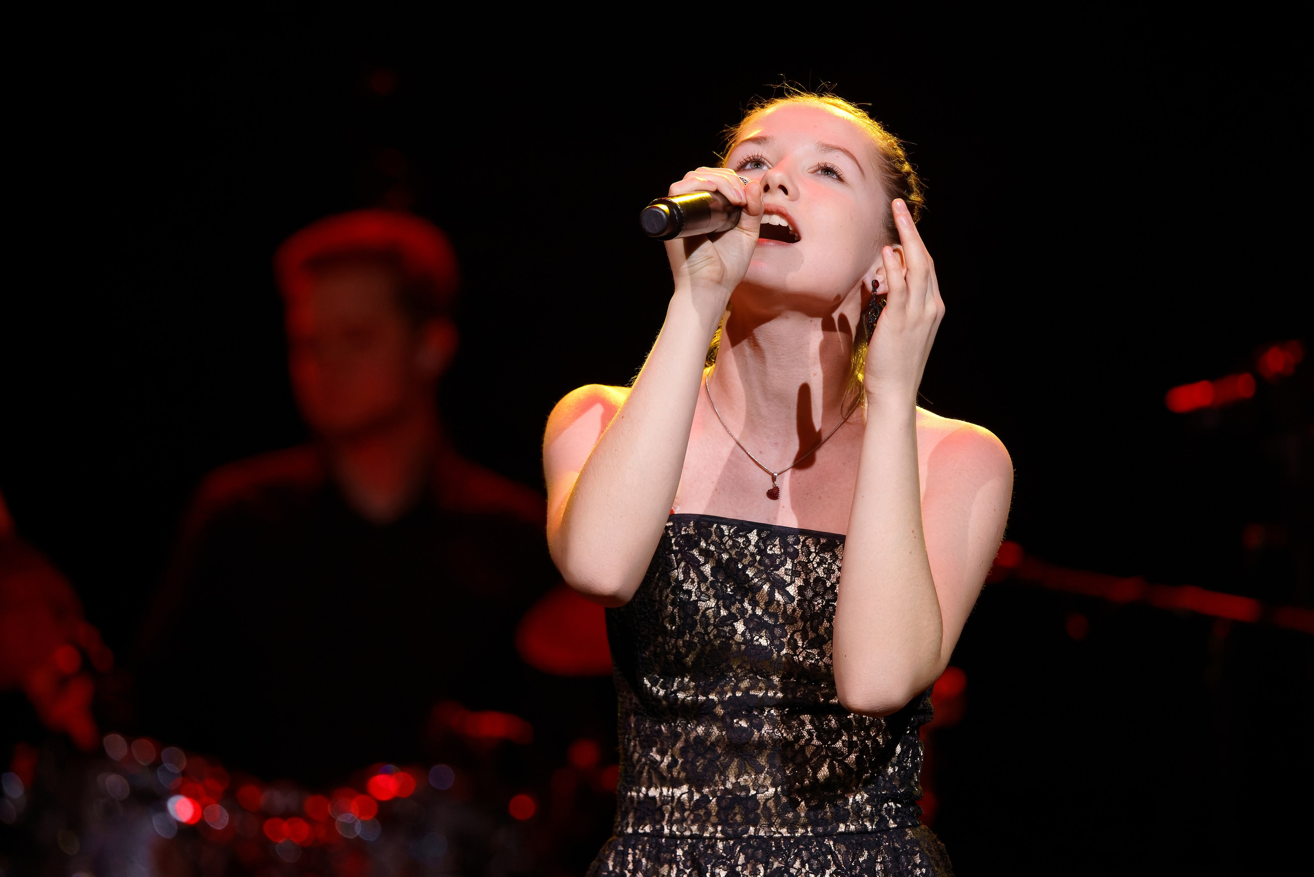 Эмоциональный портрет молодой певицы в черном кружевном платье поет с микрофоном, концертная фотография крупным планом, съемка вокалистов