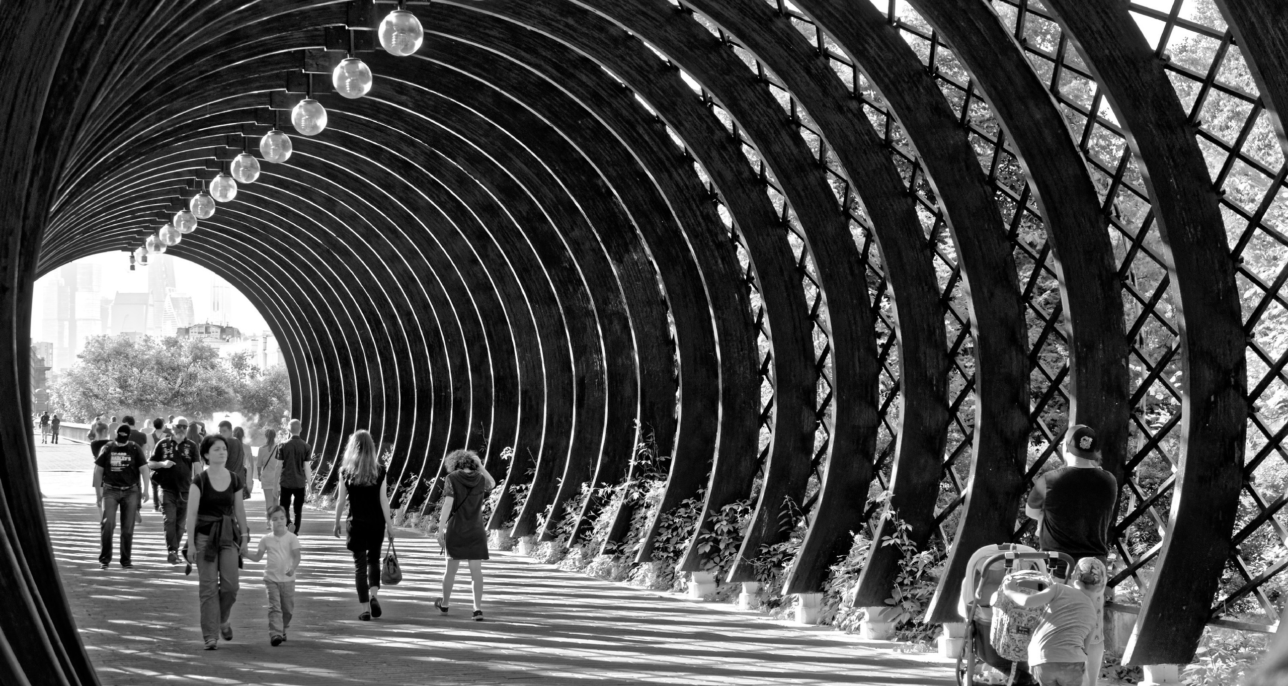 Люди идущие по арочному туннелю с повторяющимися сводами и лампами, перспектива, черно-белая архитектурная фотография