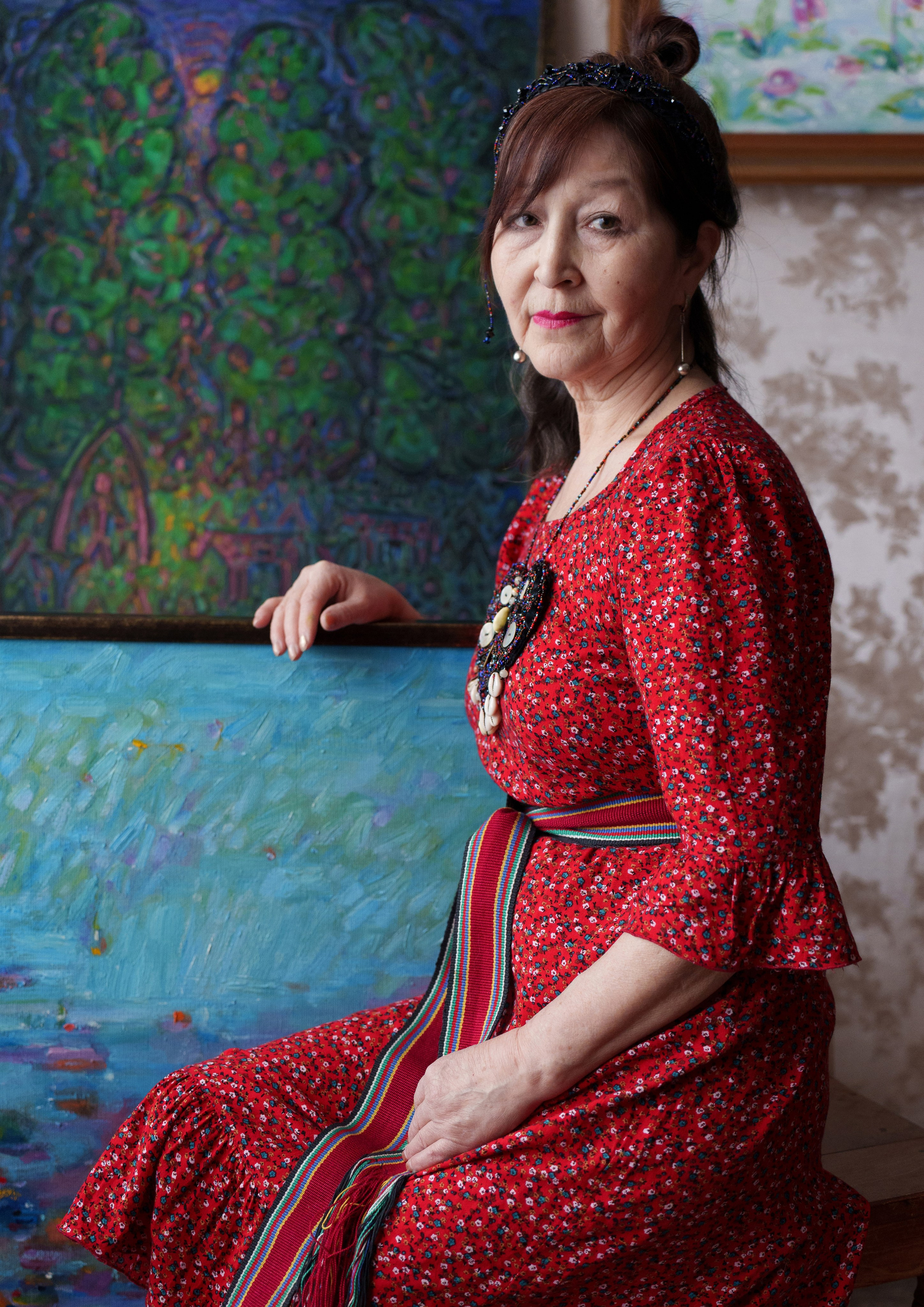 March the 7th, 2025, Lyubov Arbachakova against the backdrop of her paintings in her apartment in Tashtagol, where many of her artworks are stored.  She is the only Shor among more than 14,000 artists in Russia’s largest union — a single voice carrying the memory of her people through art.