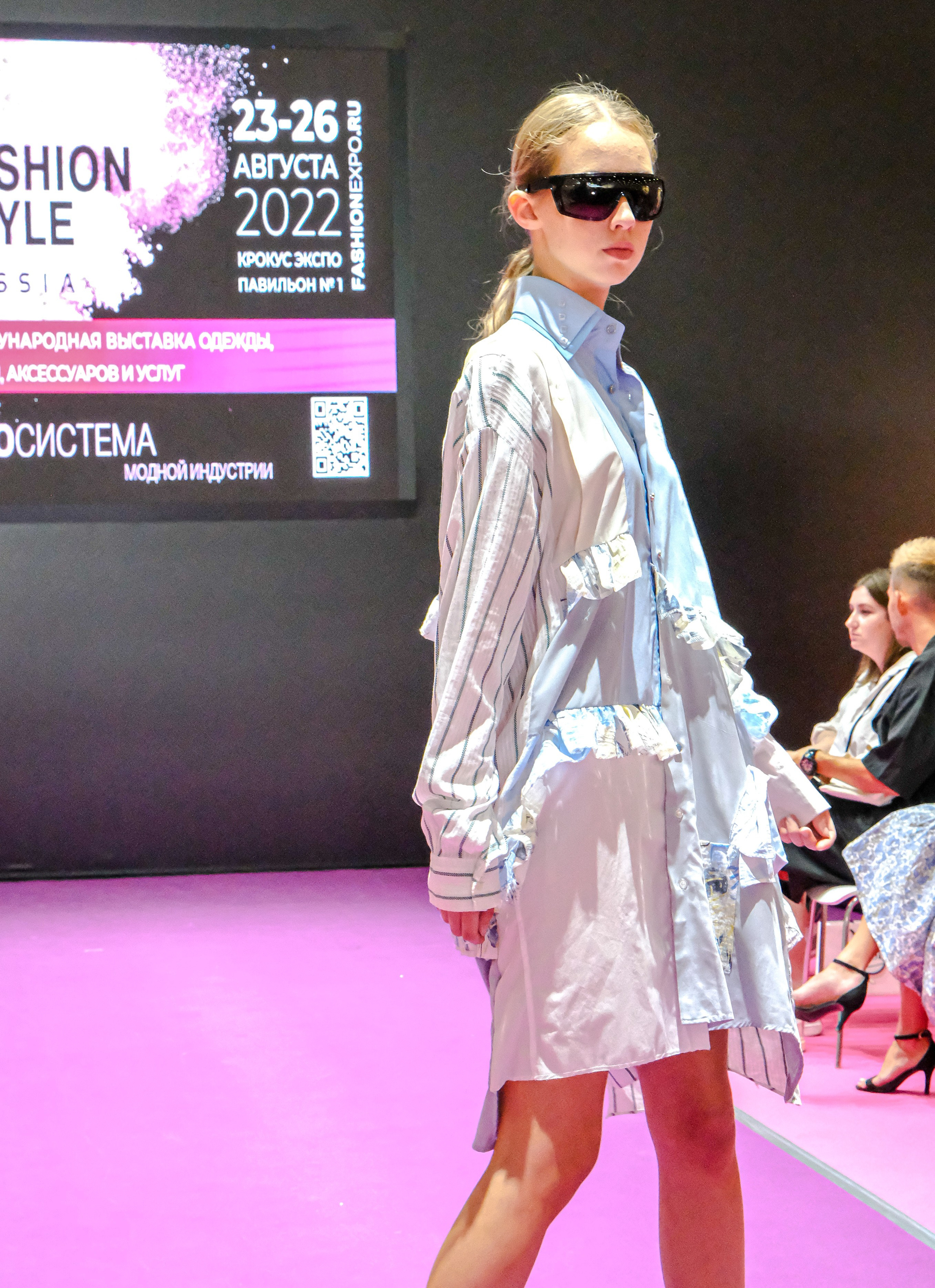  "Модели в ярких нарядах проходят по подиуму во время показа мод, освещенные яркими софитами и окруженные восторженными зрителями."