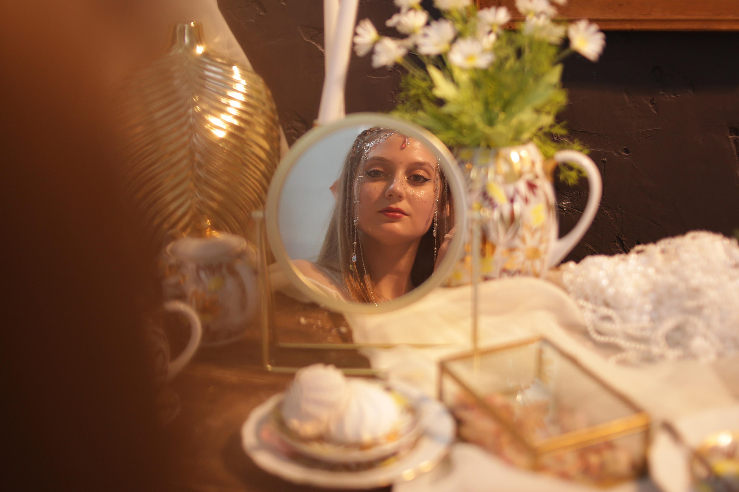 Отражение эльфийки в зеркале: девушка с ушками и головным убором смотрит в зеркало на фоне цветов и вазы