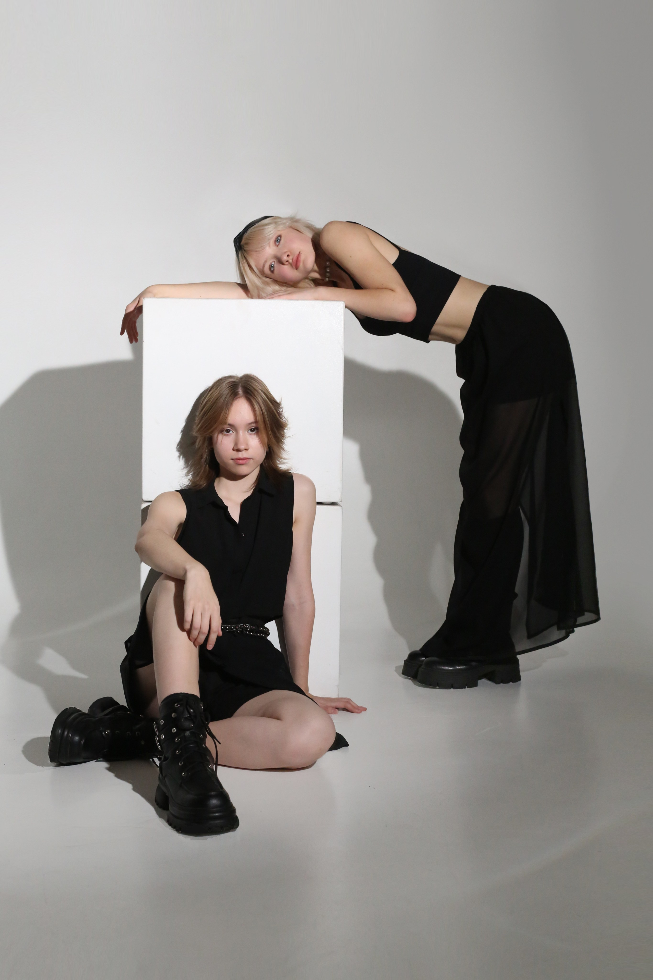 Минималистичная фотосессия: две девушки в черных костюмах позируют на белых кубах