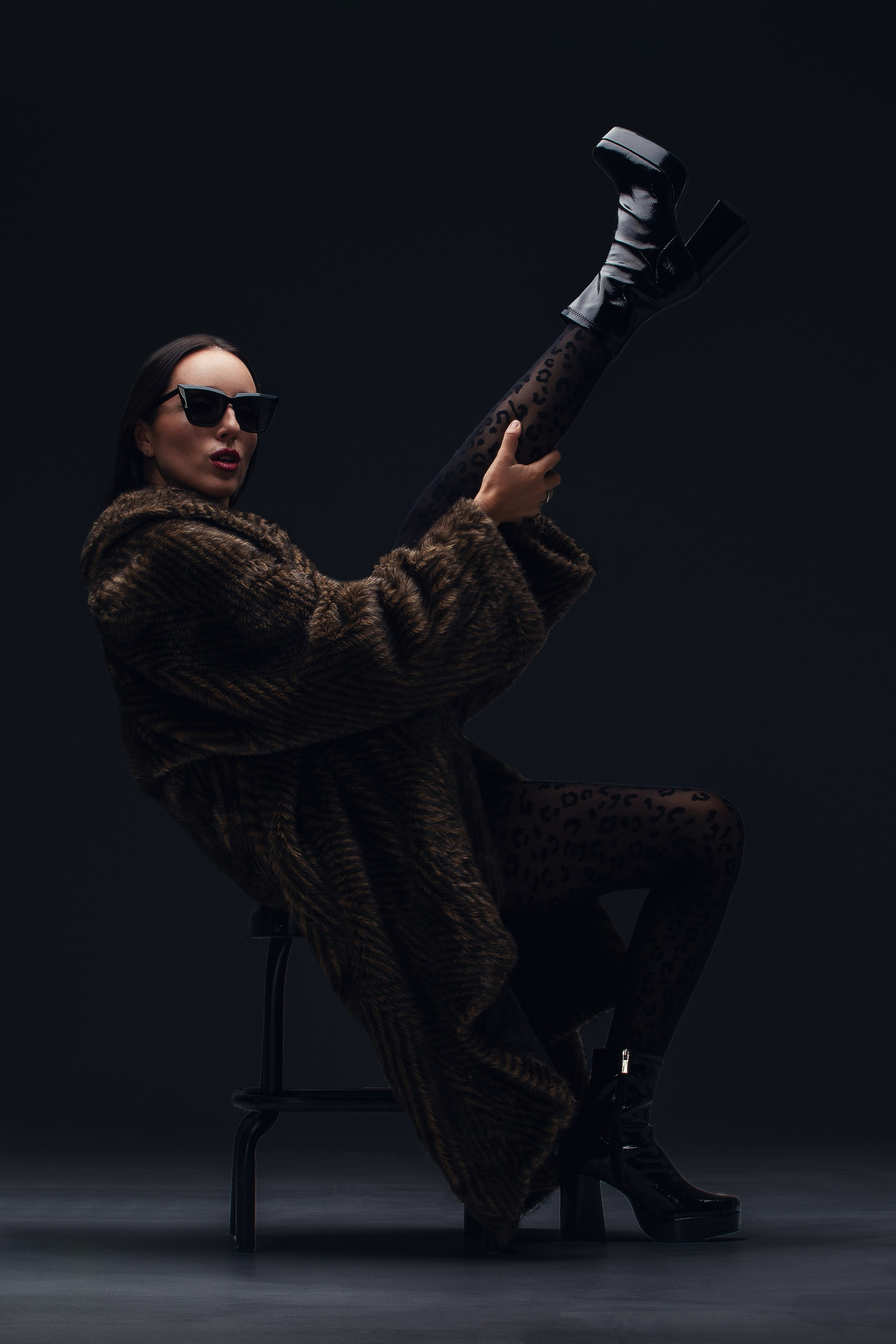 Стильный портрет женщины в леопардовом платке и меховой шубе, держащей солнцезащитные очки. Элегантный образ с ярким макияжем. Гламурный портрет: женщина в стиле ретро, сочетающем животный принт и роскошную меховую шубу. Фотография передает атмосферу шика и уверенности.