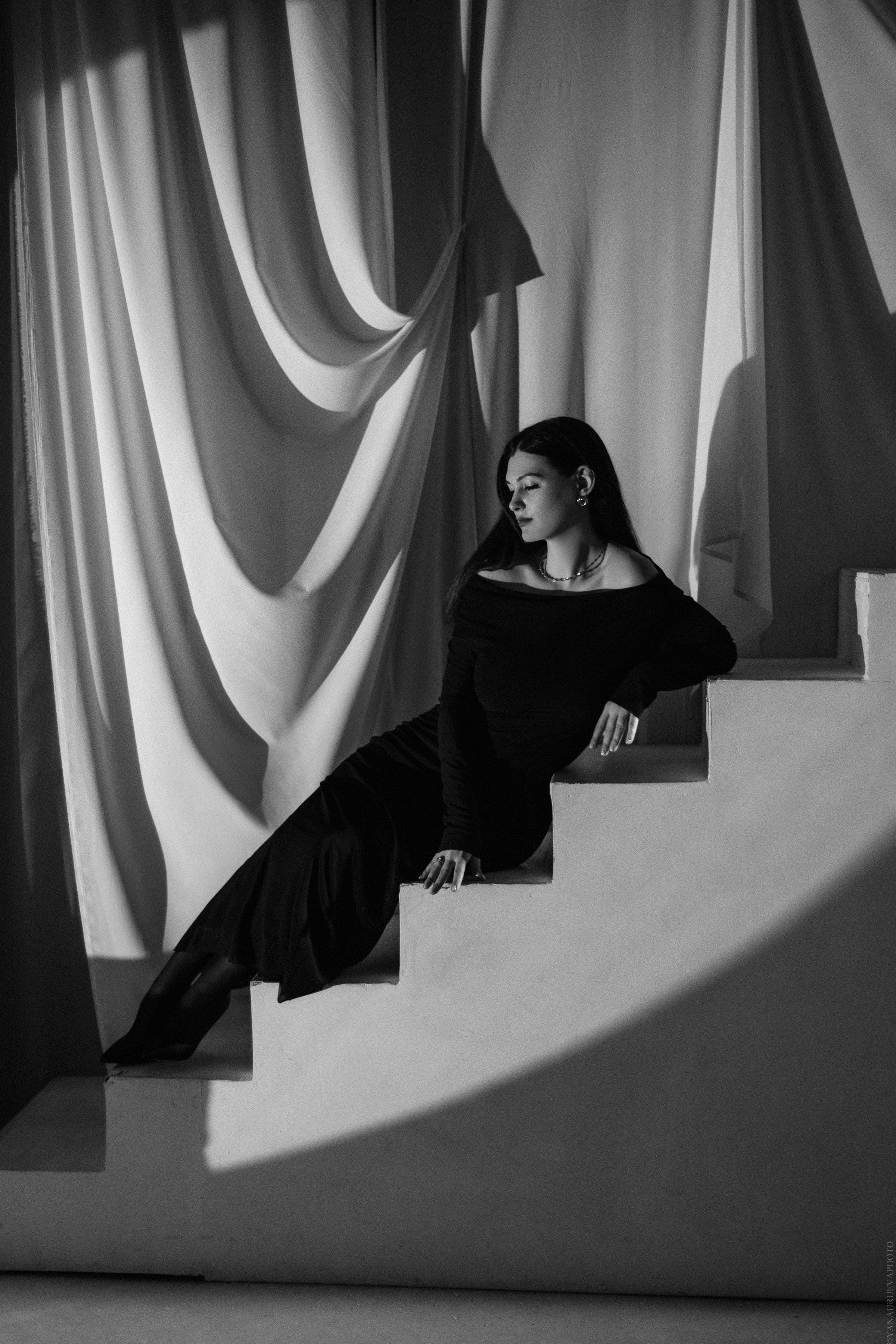 Девушка в полумраке сидит в черном длинном платье