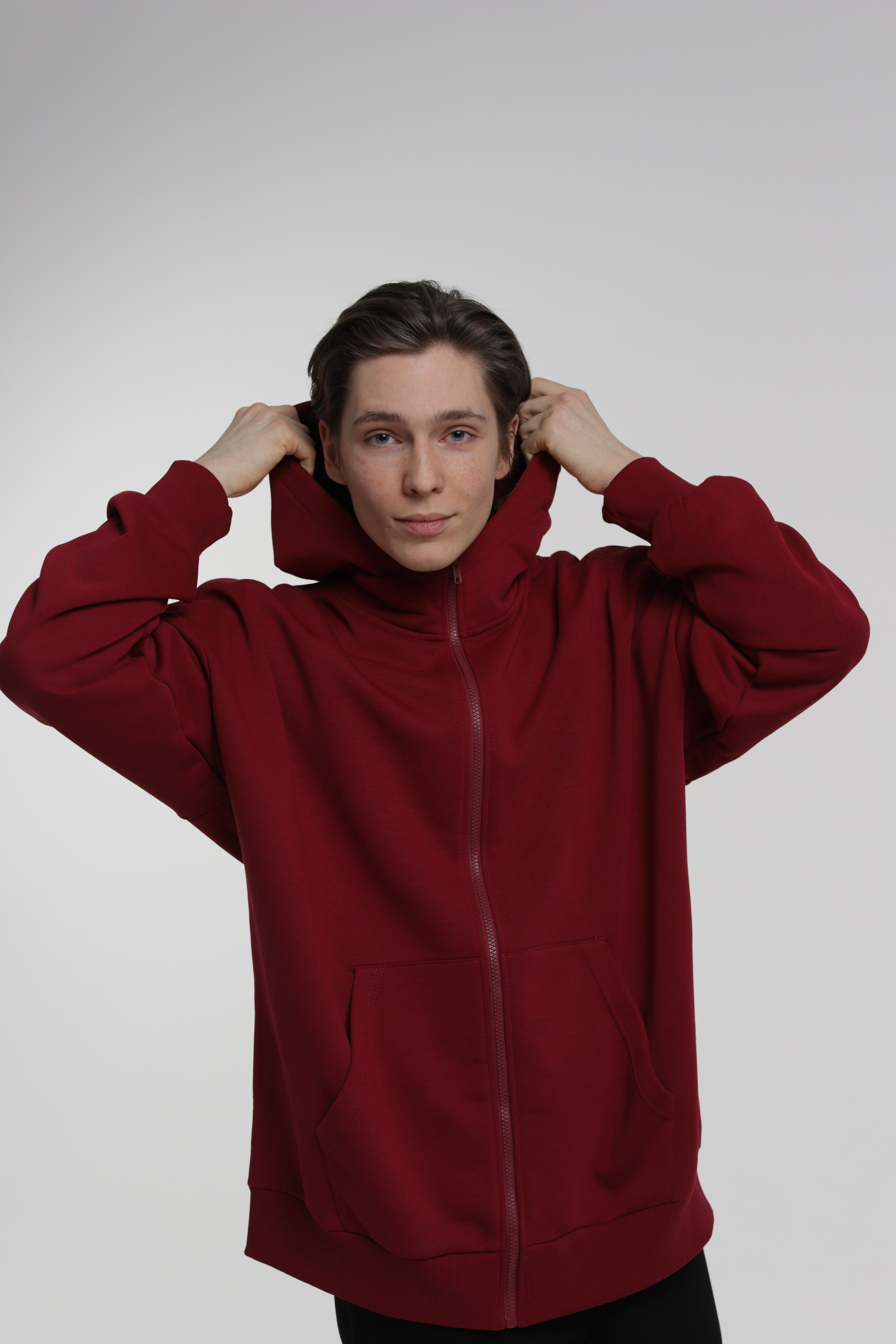 Парень модель позирует в вишневого цвета кофте на молнии с капюшоном