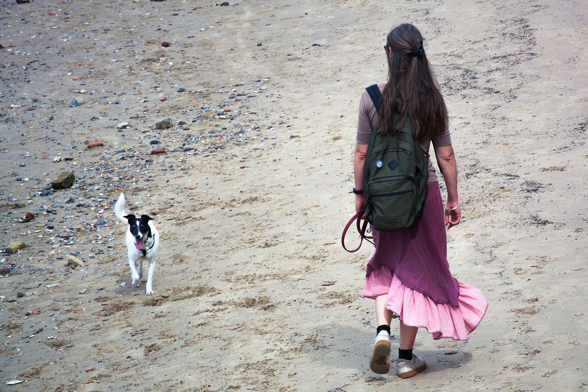 Женщина с рюкзаком и маленькая черно-белая собака гуляют по песчаному берегу Темзы в Лондоне.