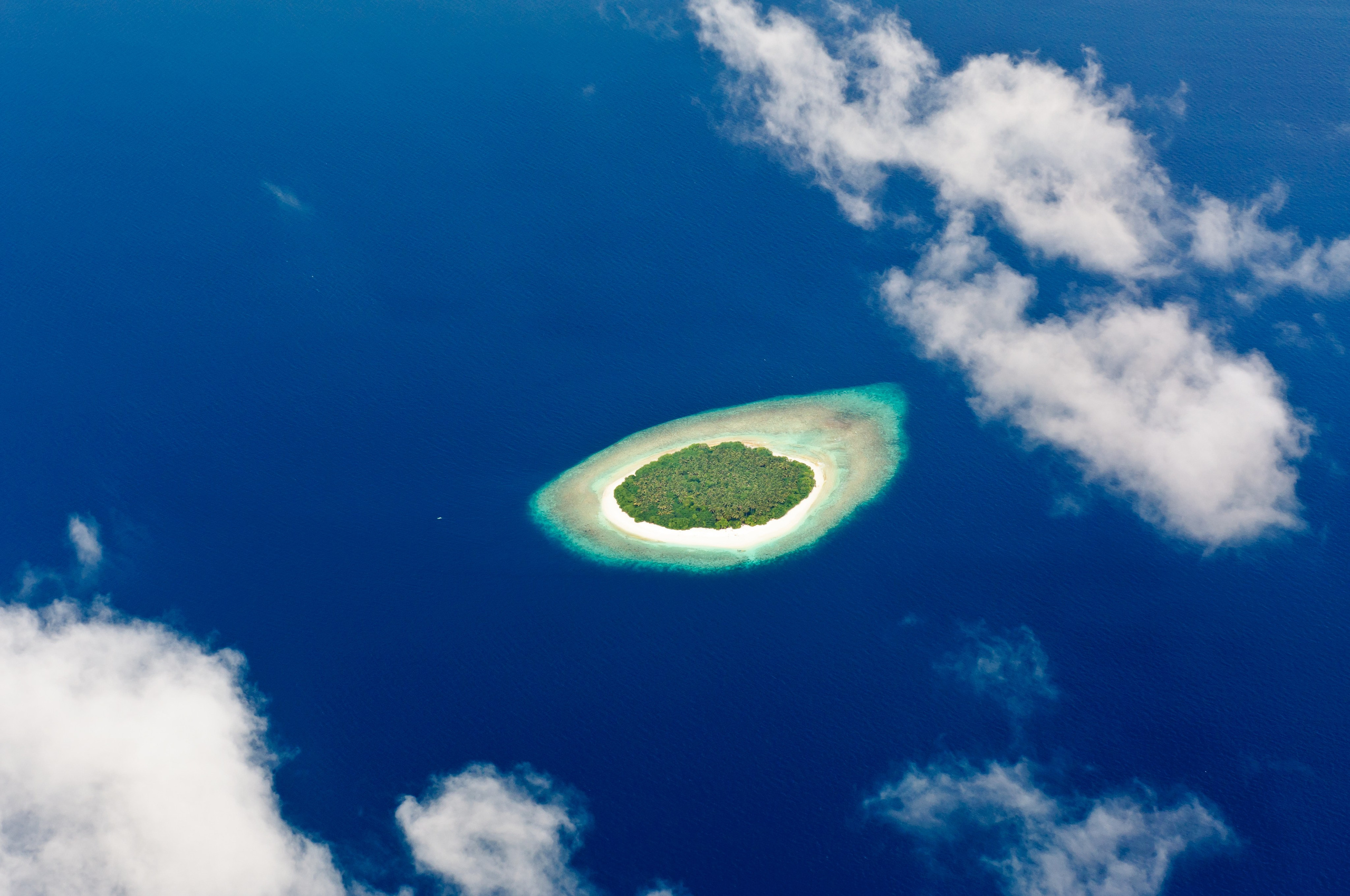 Вид с воздуха через облака на остров и лагуну. Мальдивы
