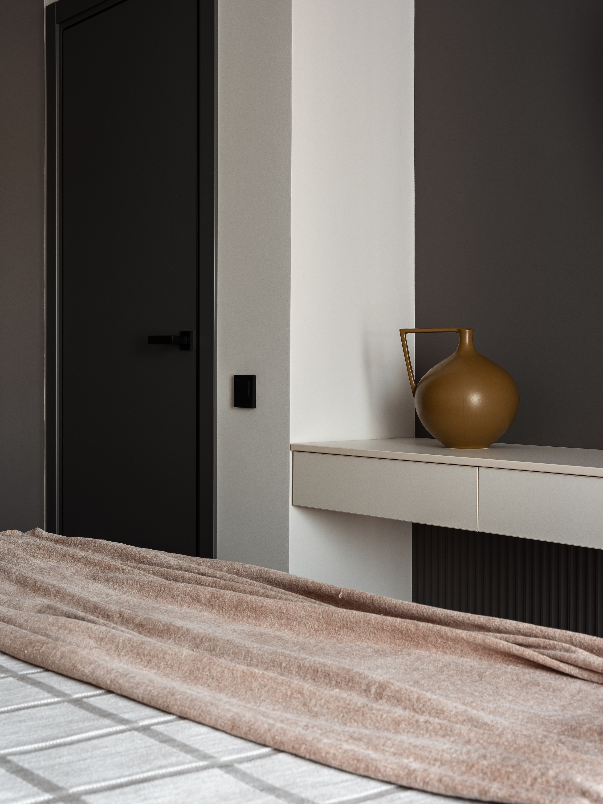 Минималистичная спальня с черной дверью и белой консолью, украшенной керамической вазой в теплых оттенках, дизайнер Екатерина Мищенко, фотограф Сергей Денисенко, интерьер в спокойной палитре с акцентами и современными деталями.