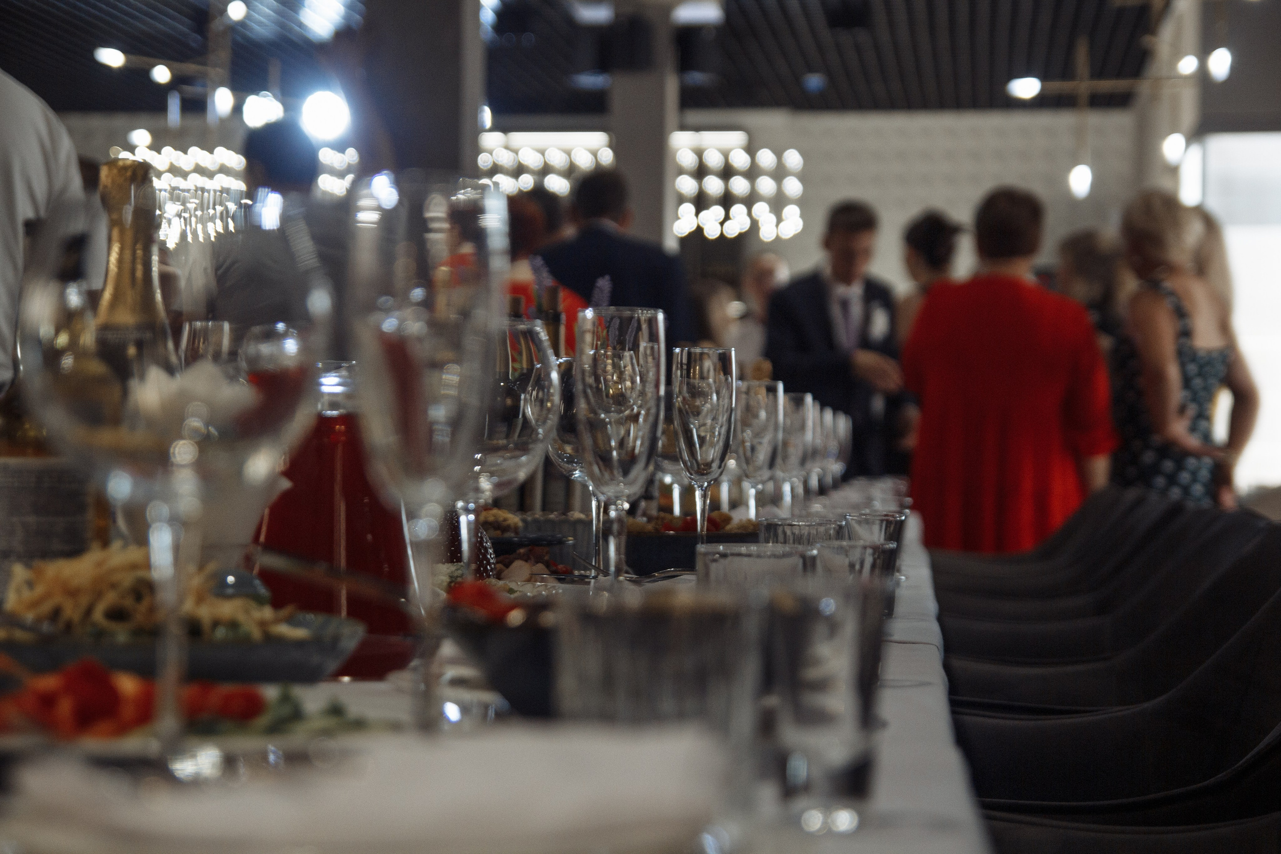 Репортажная фотография свадебного банкета — сервировка стола, бокалы, гости в разгаре праздника.