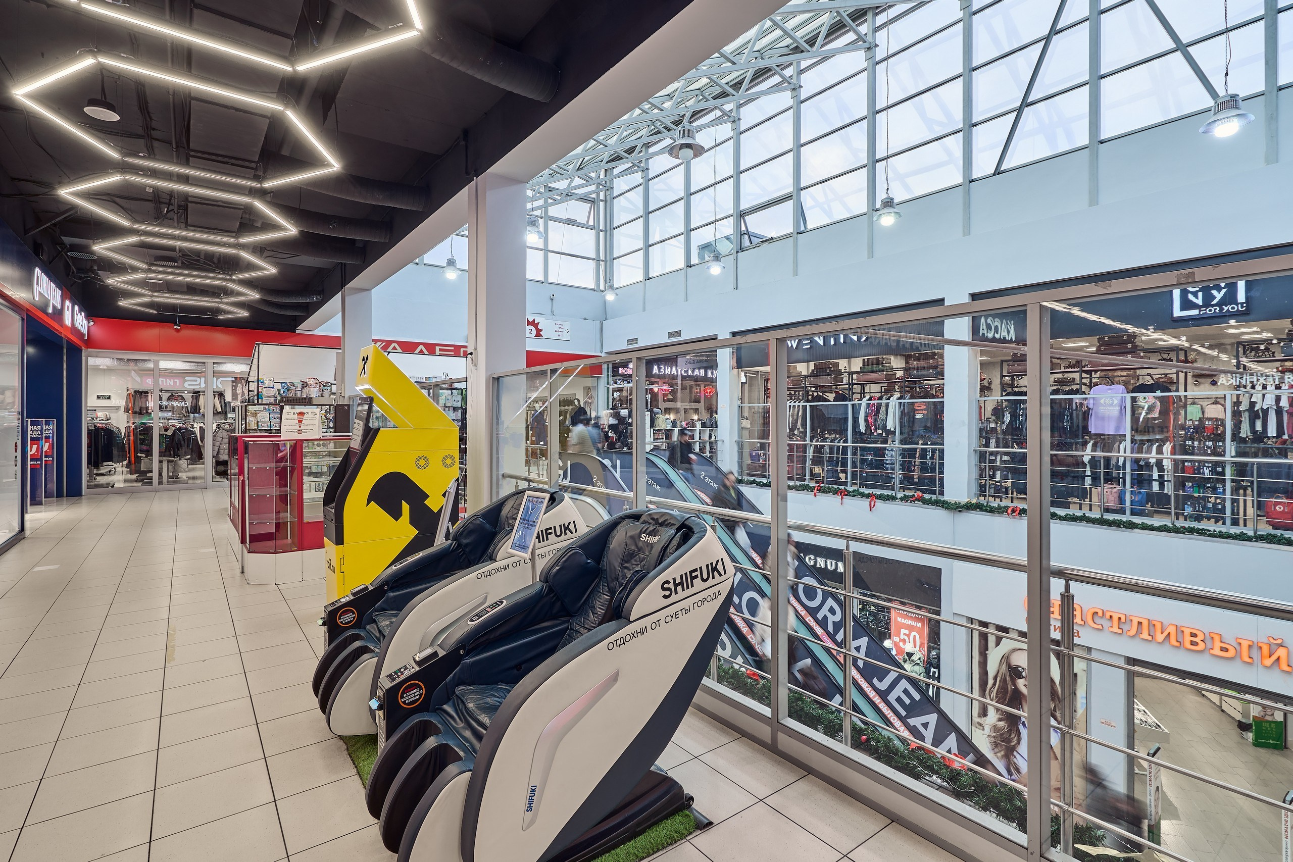 Интерьерное фото второго этажа торгового центра в Раменском с массажными креслами, банкоматом, видом на креативное освещение ТЦ и фонарь для поступления естественного света