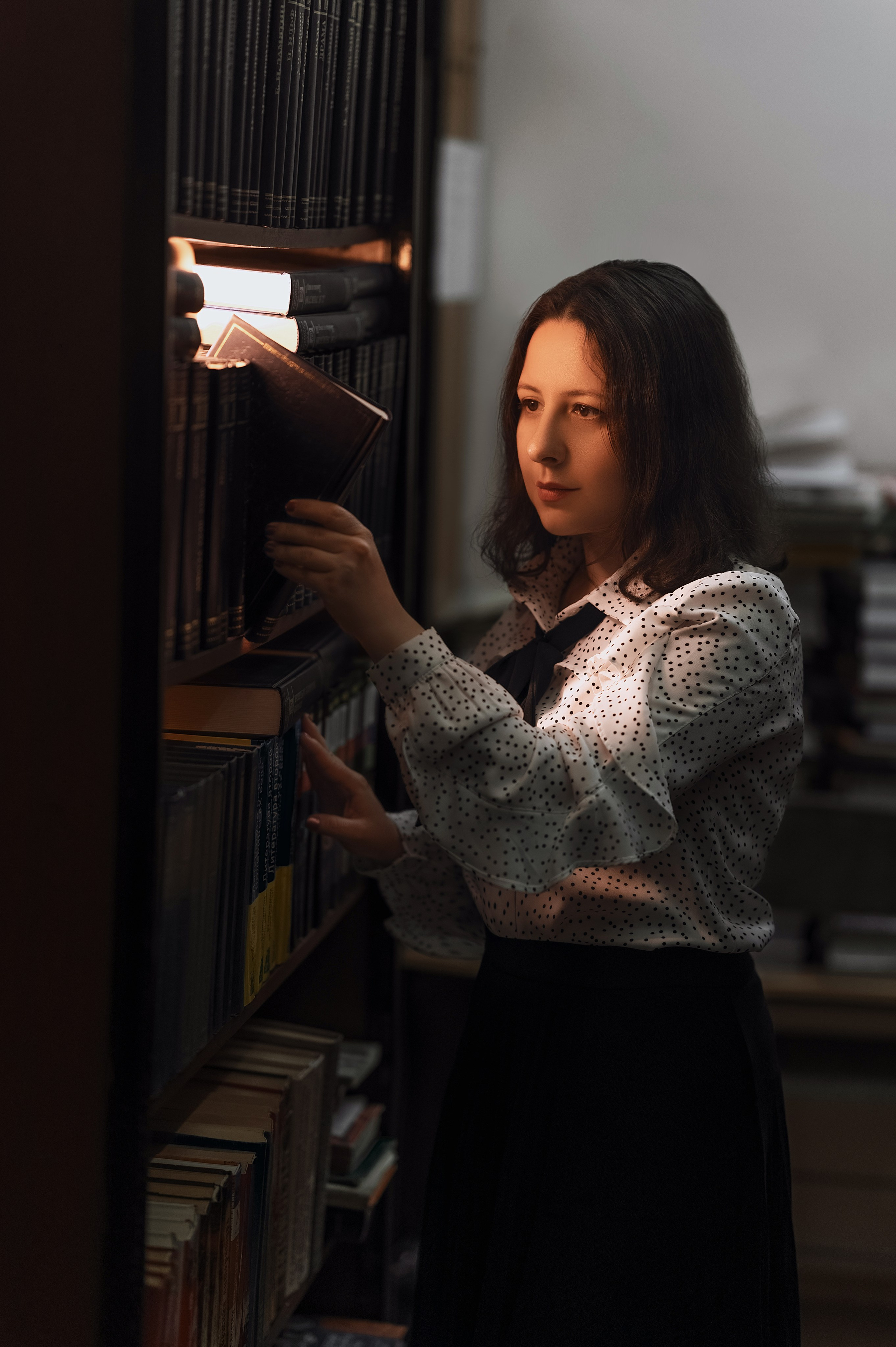 Библиотека как фотолокация: девушка в светлой блузке и тёмной юбке между стеллажами. Фото от Елизаветы Жуйковой (Волгодонск).
