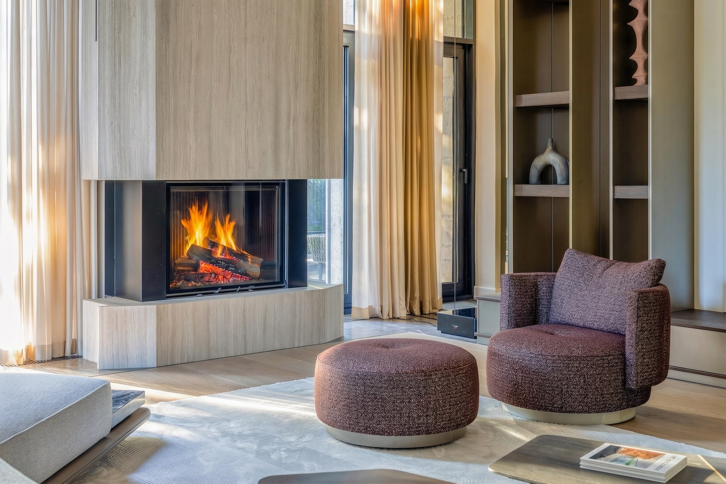 Деталь интерьера гостиной с современным трехсторонним камином, дизайнерским креслом винного цвета и панорамным видом, проект Валерии Котович в Подмосковье.