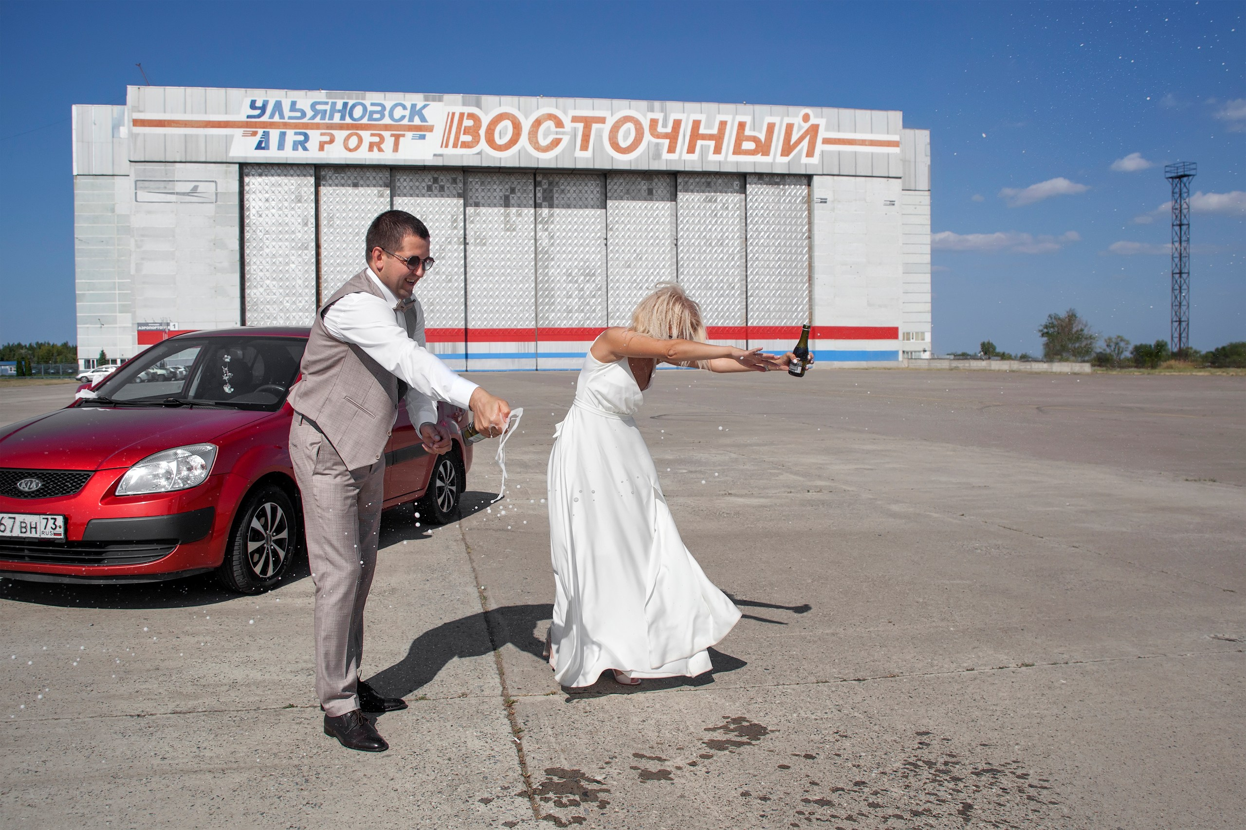 жених с невестой обливаются шампанским на вытянутых руках - свадебная прогулка в аэропорт