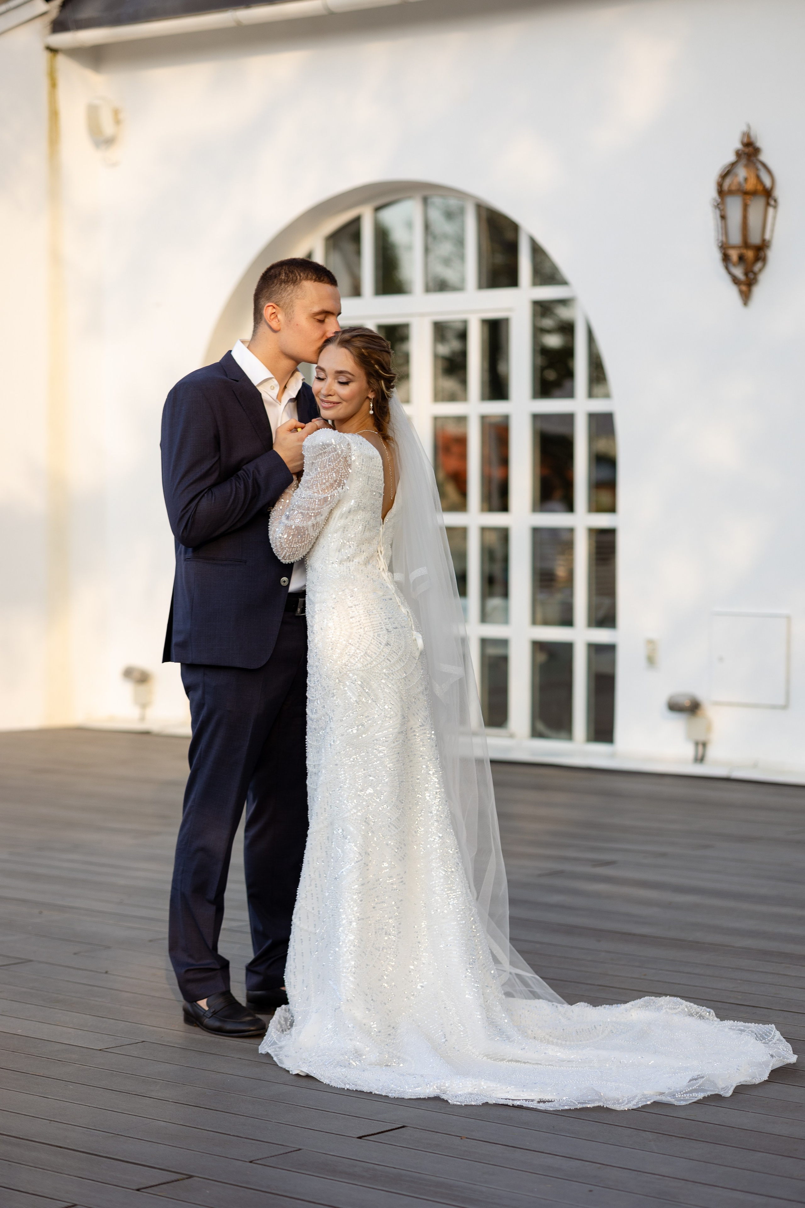 Молодые прижались друг к другу на фоне стены и окна.