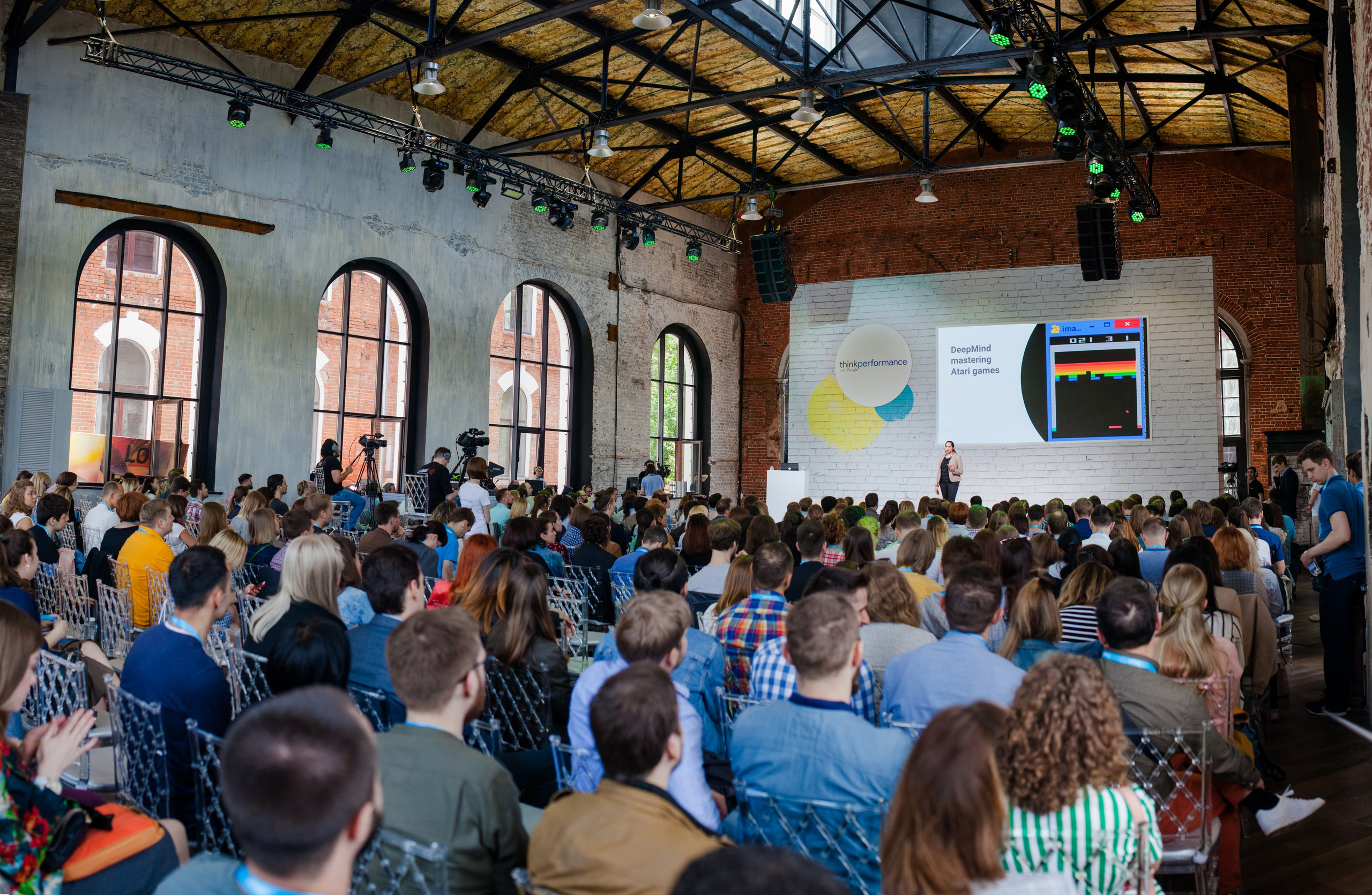 Большое количество зрителей смотрит на сцену где спикер показывает презентацию