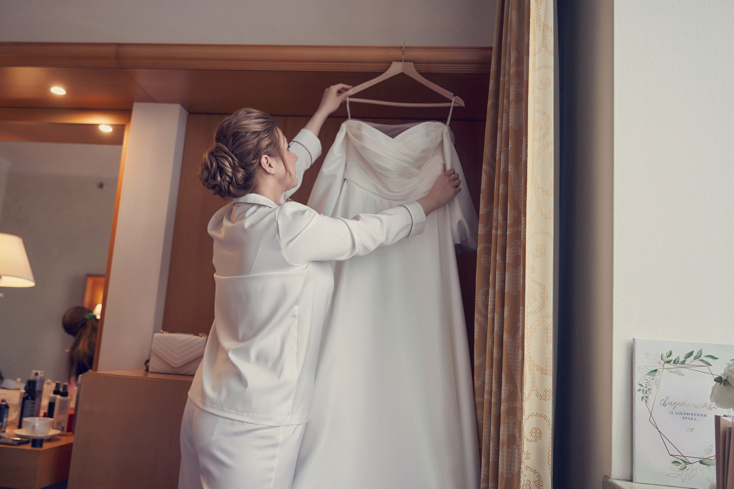 девушка берёт свадебное платье с вешалки что бы надеть 