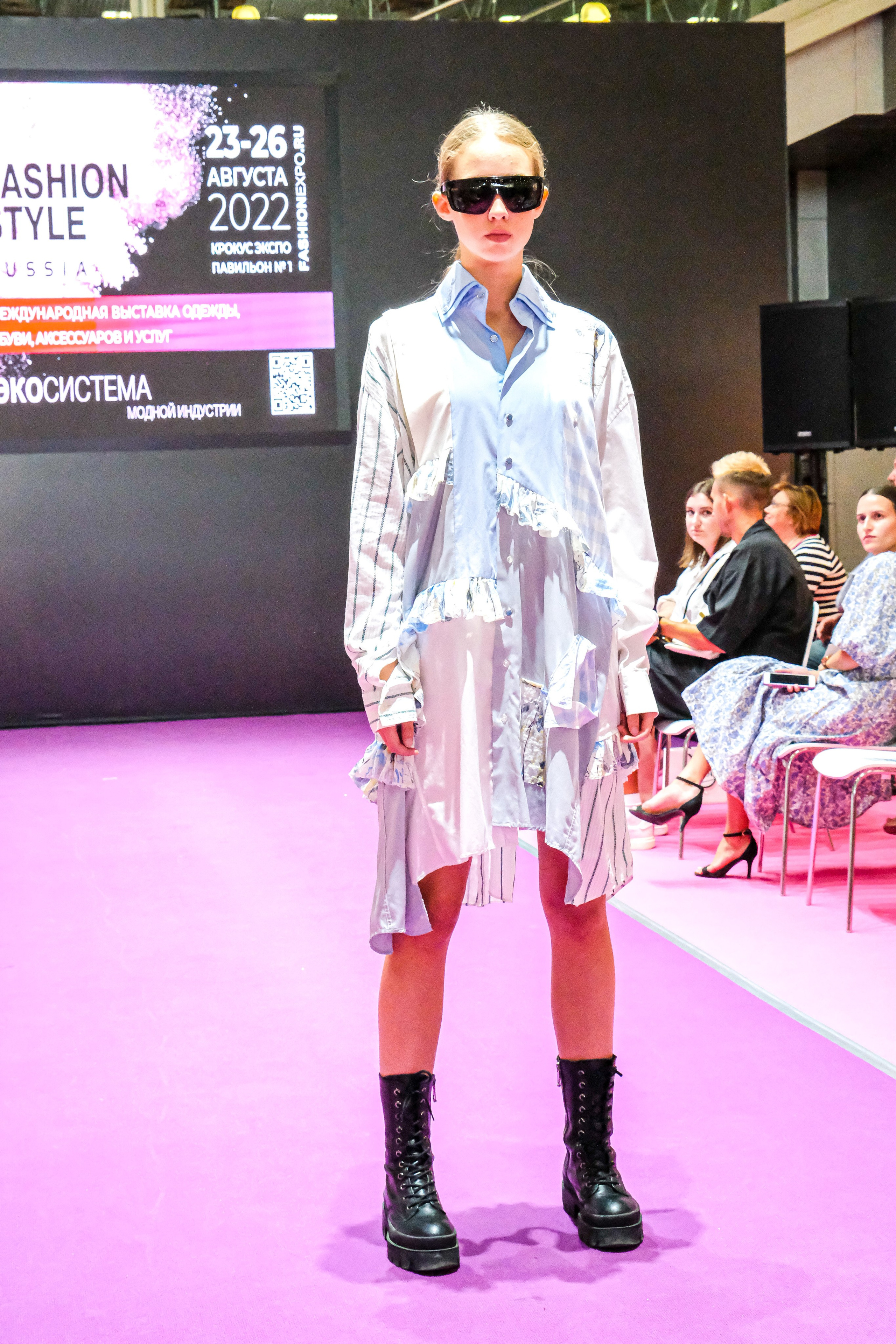  "Модели в ярких нарядах проходят по подиуму во время показа мод, освещенные яркими софитами и окруженные восторженными зрителями."