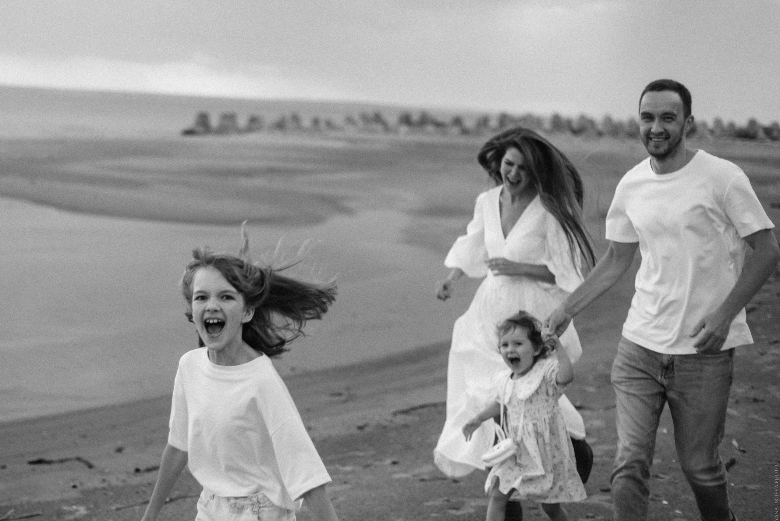 Семья бежит по пляжу на закате черно-белая фотография
