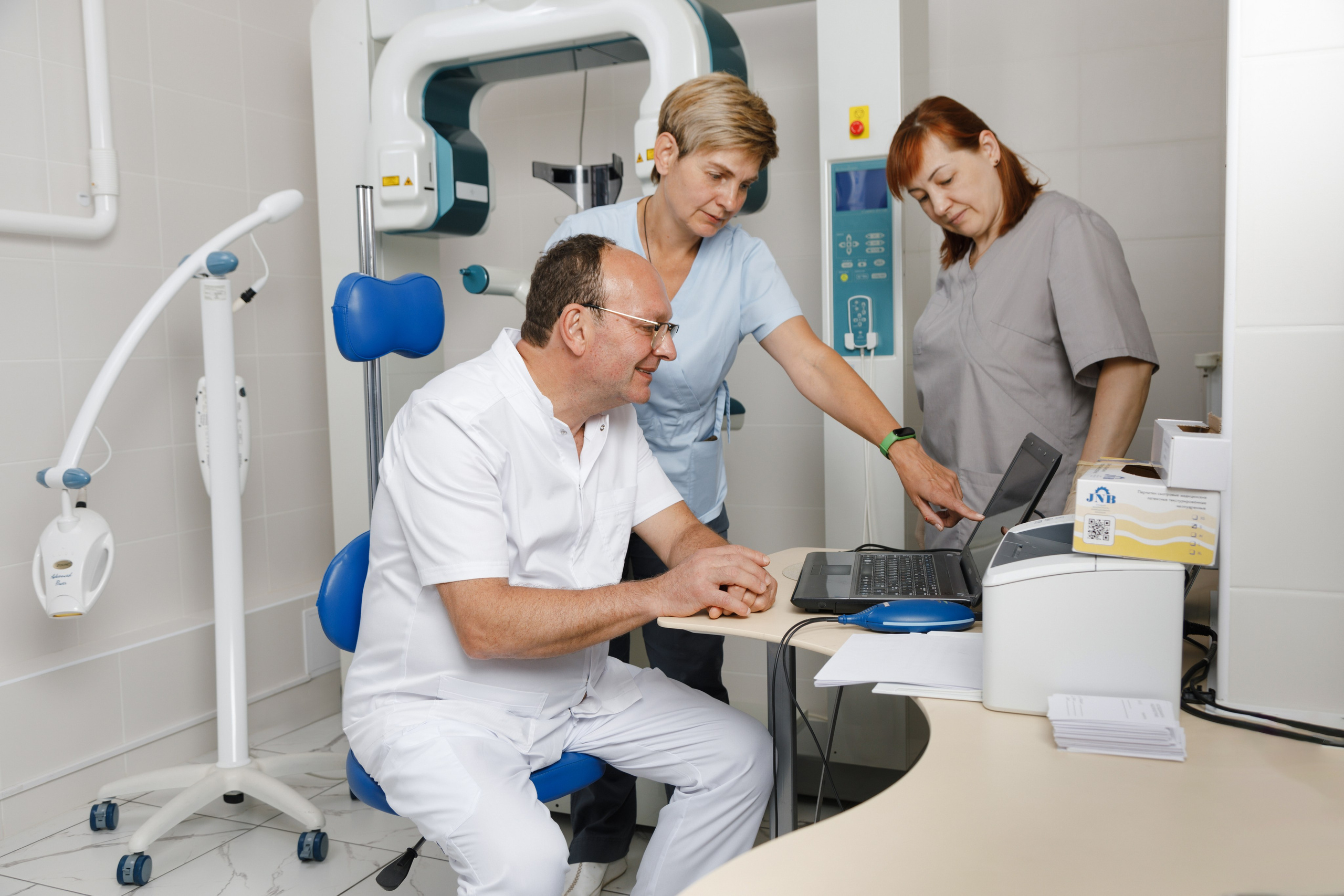 Врач и две медсестры изучают рентген-снимки и анализы пациента для планирования лечения.