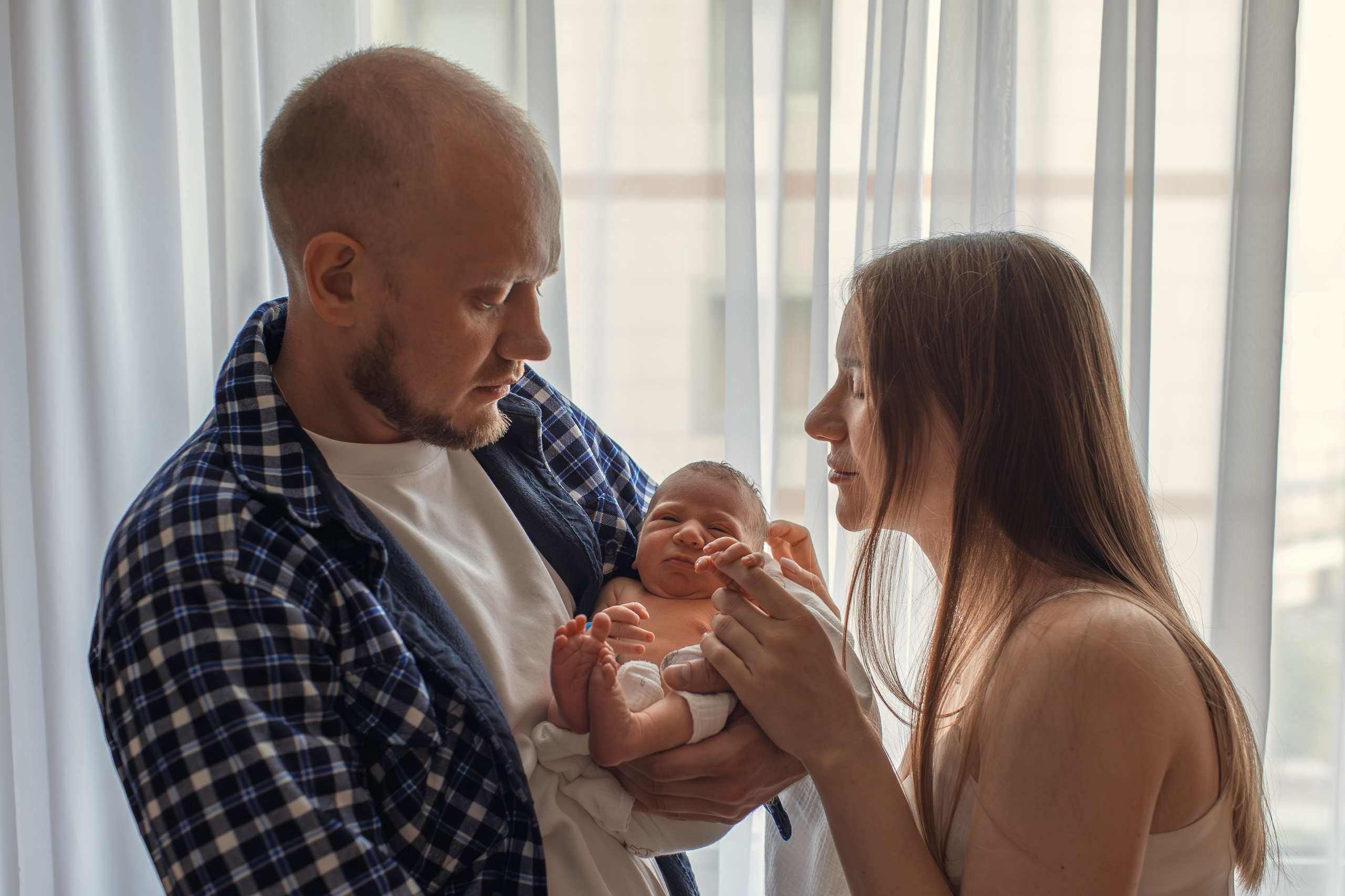 Счастливая семья втроём: родители смотрят на новорождённого ребёнка.