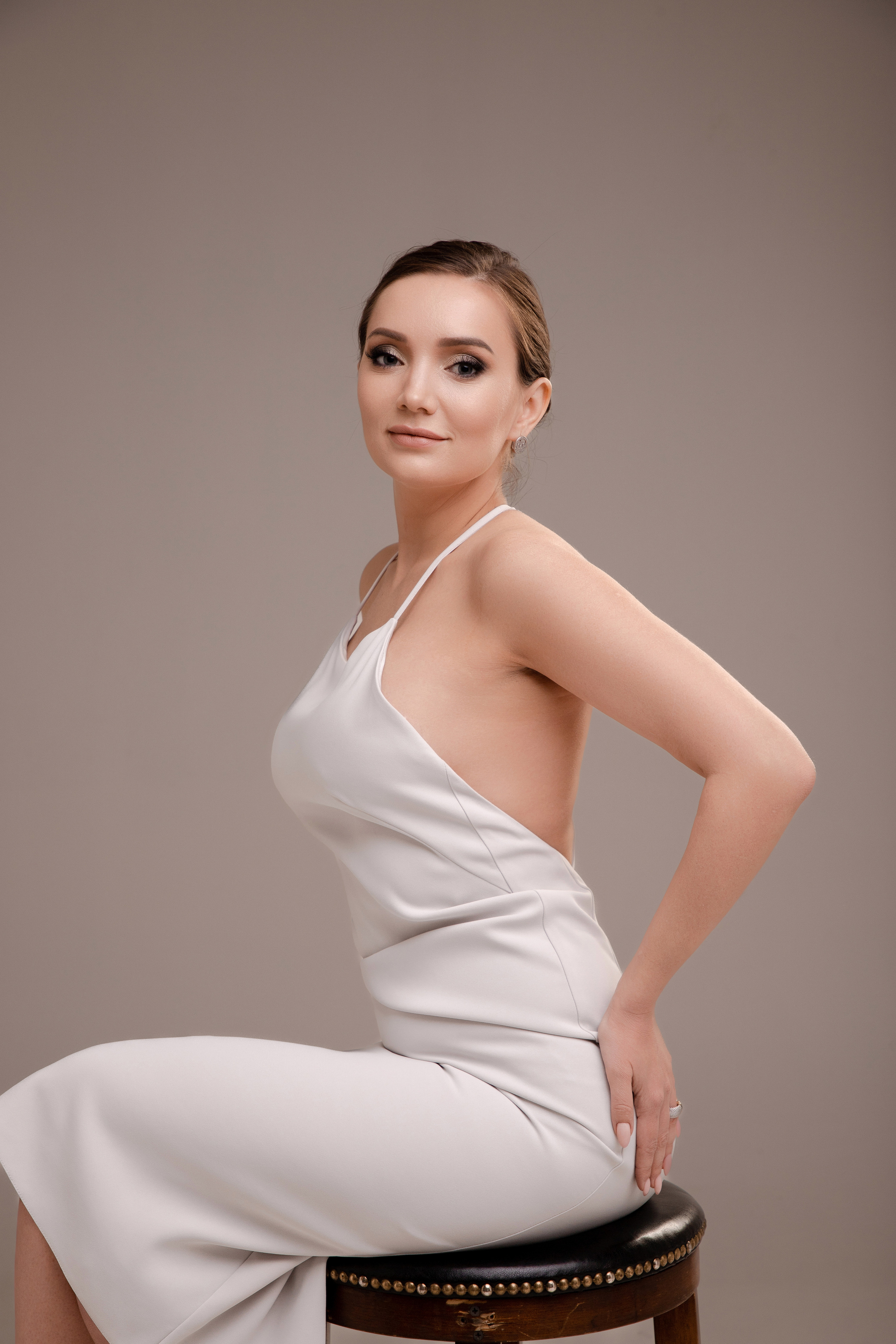 Студийная фотография девушки сидящей на барном стуле на циклораме в теплой гамме в шелковом белом платье комбинации