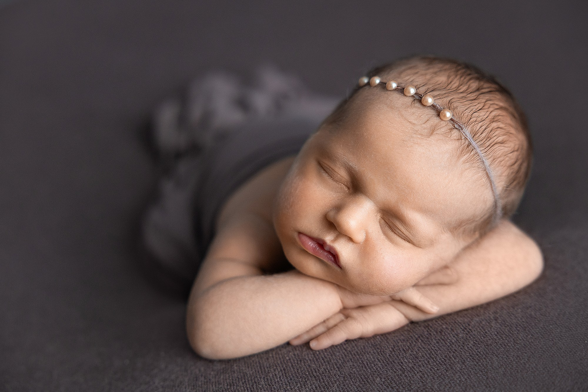 Новорожденная девочка в повязке с бусинками спит на животике.