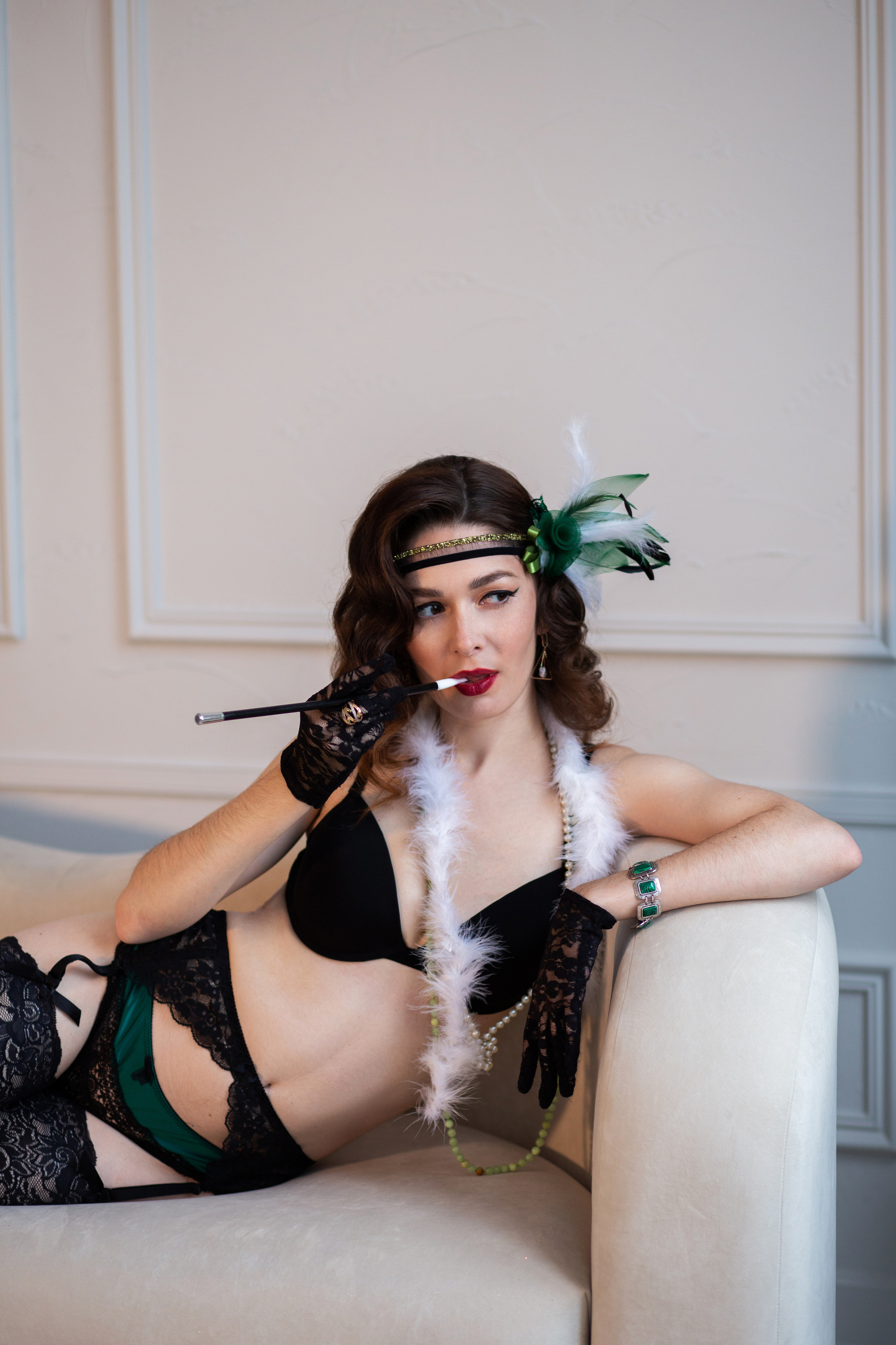 Девушка  одетая   в стиле Гетсби лежит на  белом  диване. У нее в руках  мундштук.