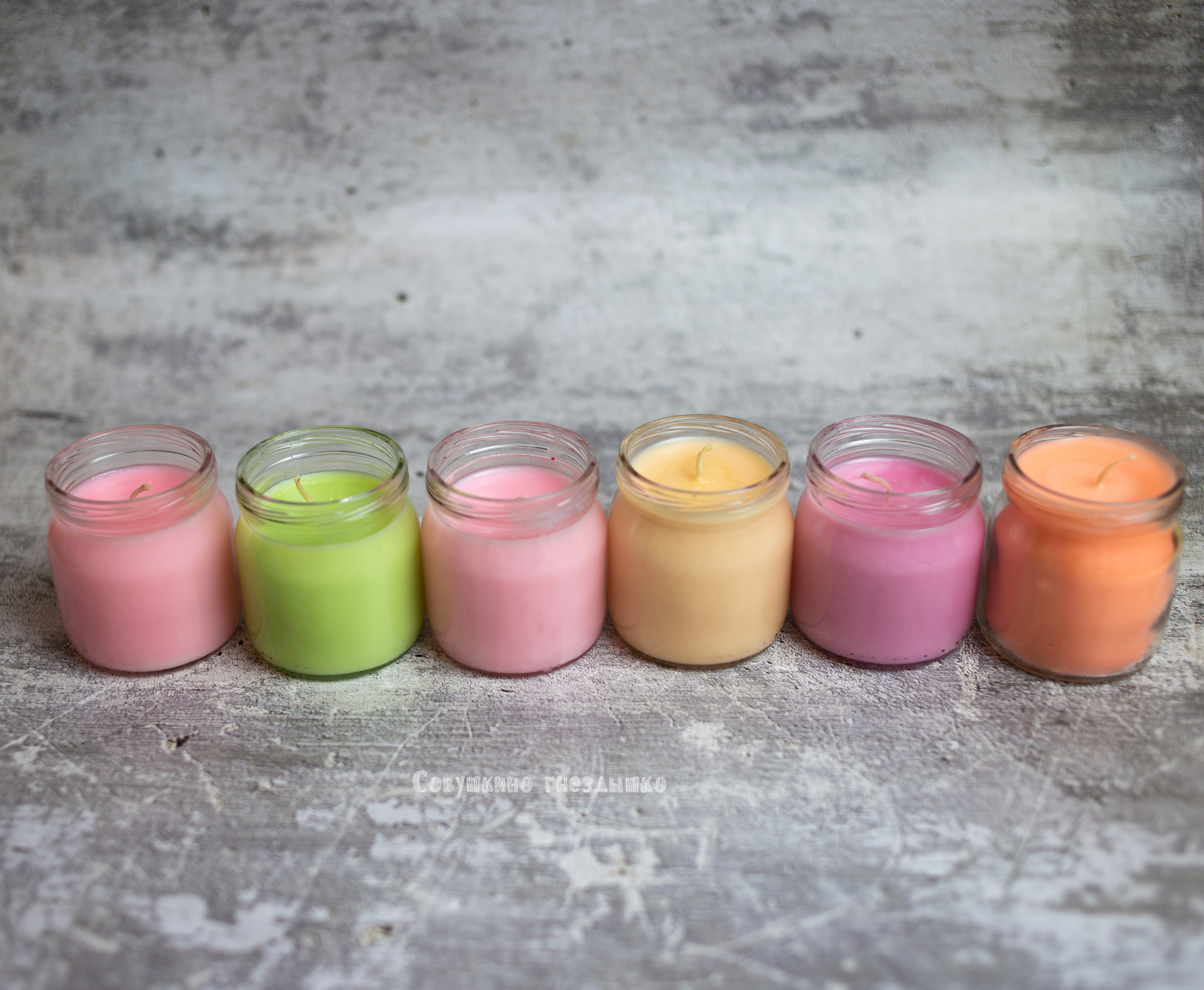 соевые свечи  в  баночках  выстроились  в ряд. свечи разных  цветов. фон  бетон.