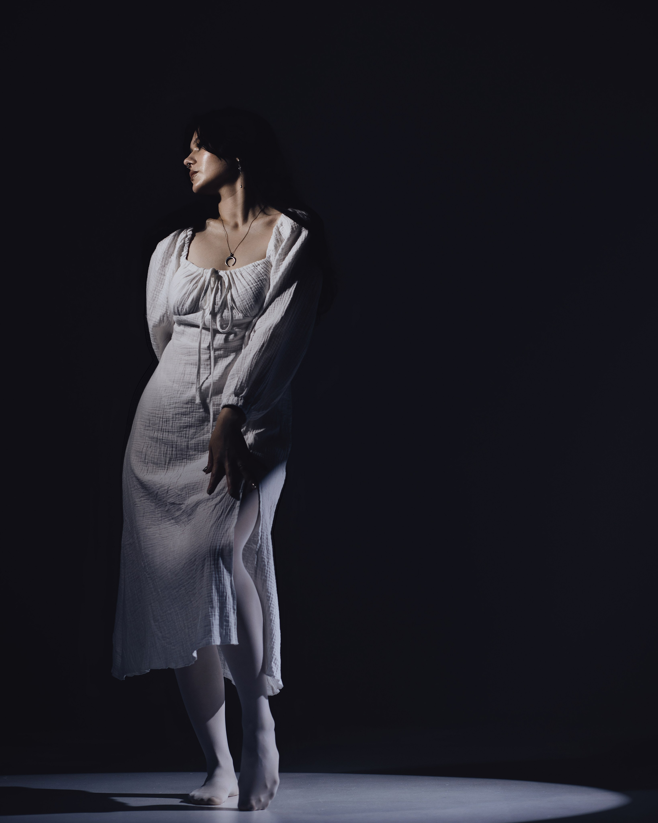 Александра Овечкина, Пенза: модель в белом платье стоит в узком луче света на черном фоне, театральная атмосфера.