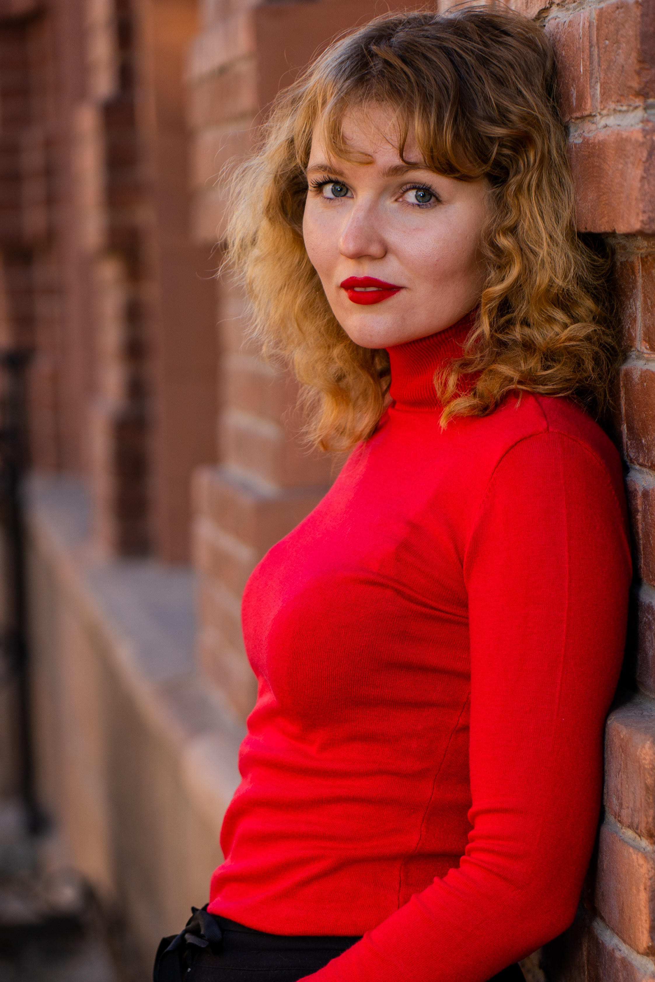 Красивый снимок девушки с кудрями возле стены в редких оттенках цвета