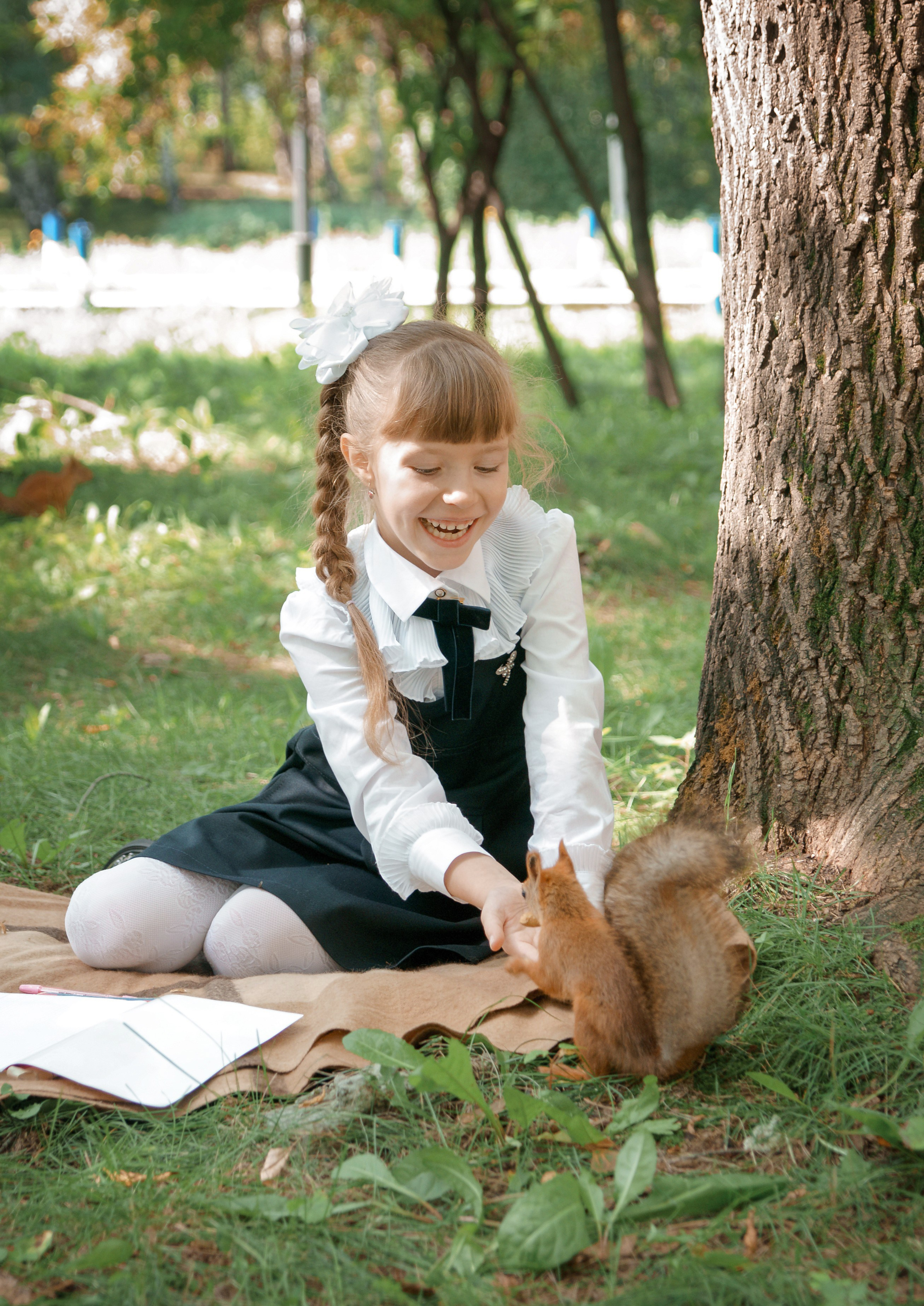 Детская фотосессия осенью - школьница сидя у дерева подзывает белку