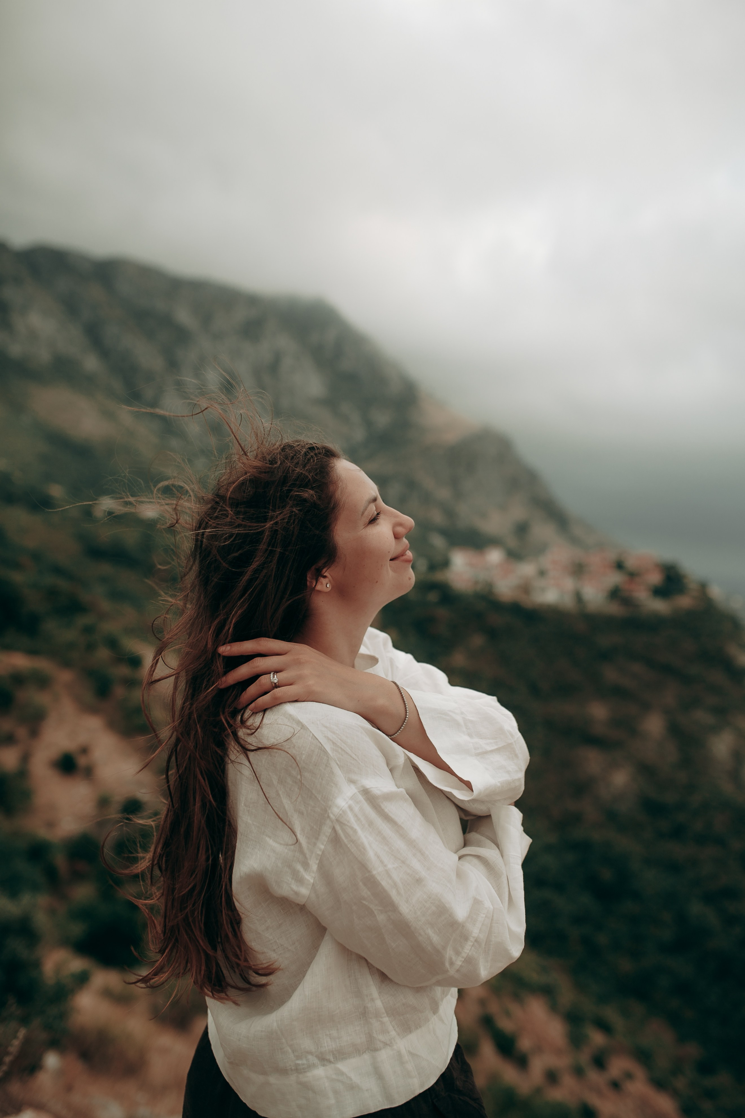 Женская фотография в движении на фоне гор и моря в пасмурную погоду. Девушка в Черногории на смотровой площадке в Будве с видом на горы