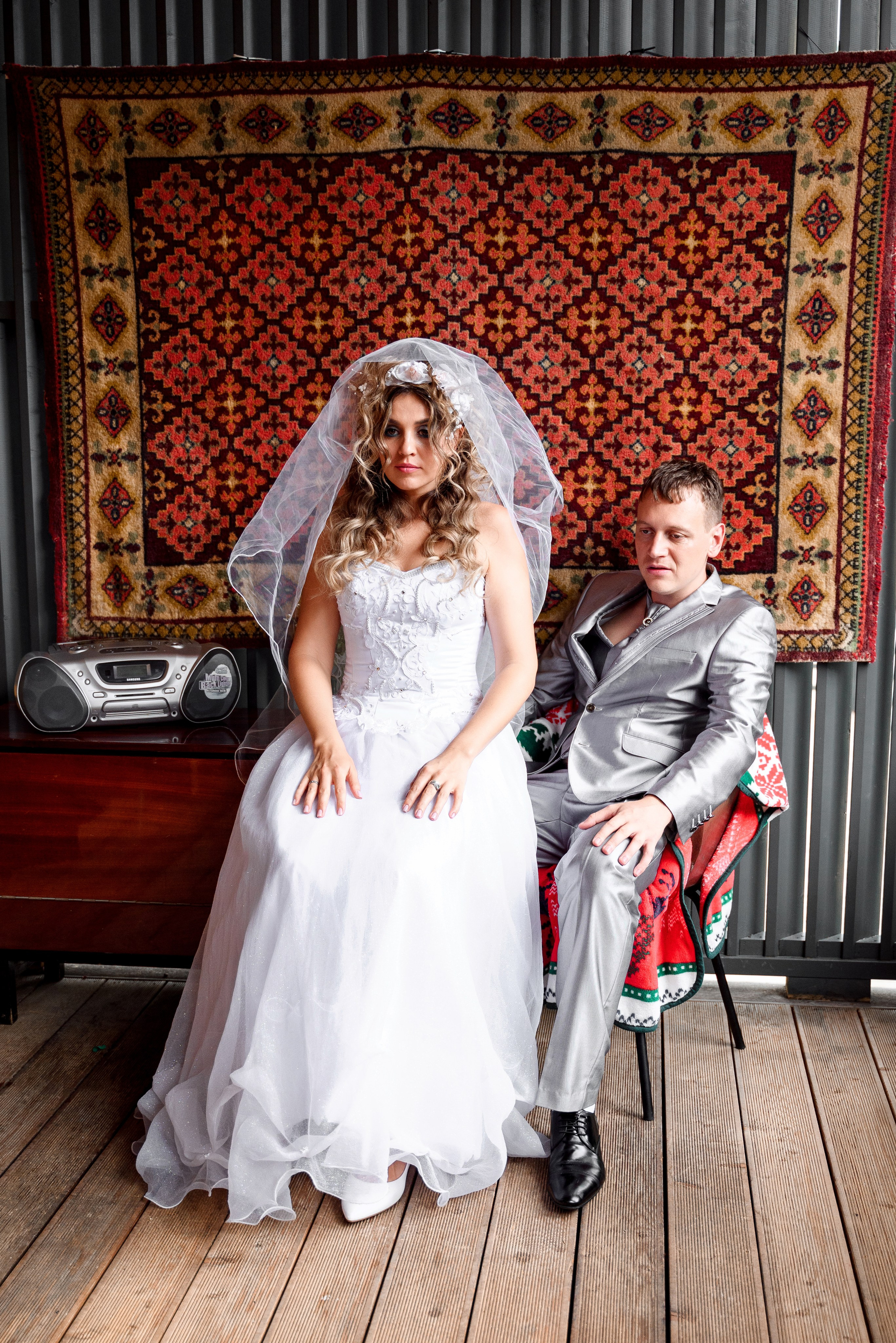 Стиль 90-х, яркие цвета и необычные аксессуары — свадебная фотосессия в Сочи муж и жена сидят напротив ковра муж кресле она на колени 