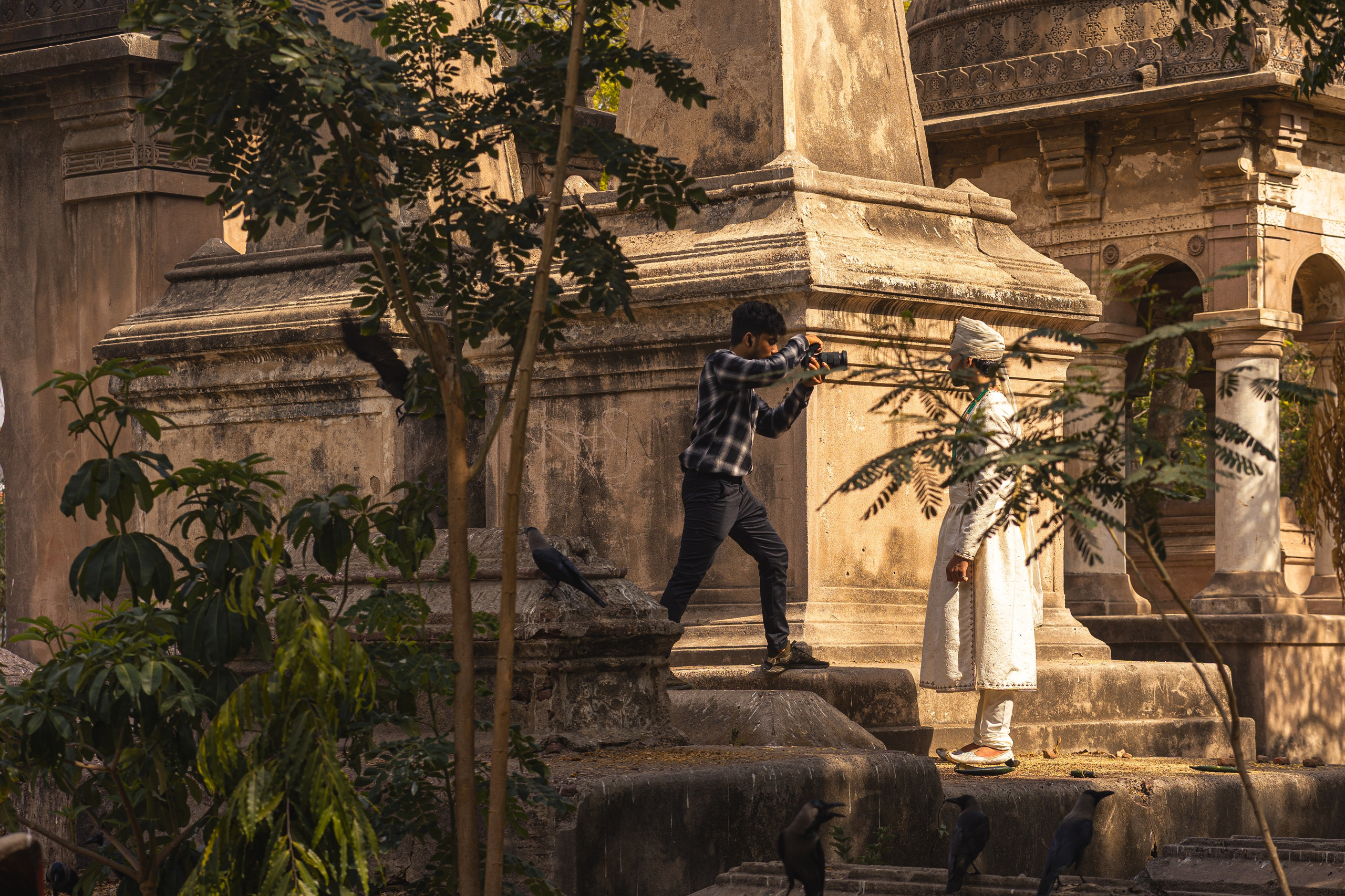 Древнее каменное здание среди зелени и деревьев. Фотограф снимает переодетого в исторический костюм мужчины