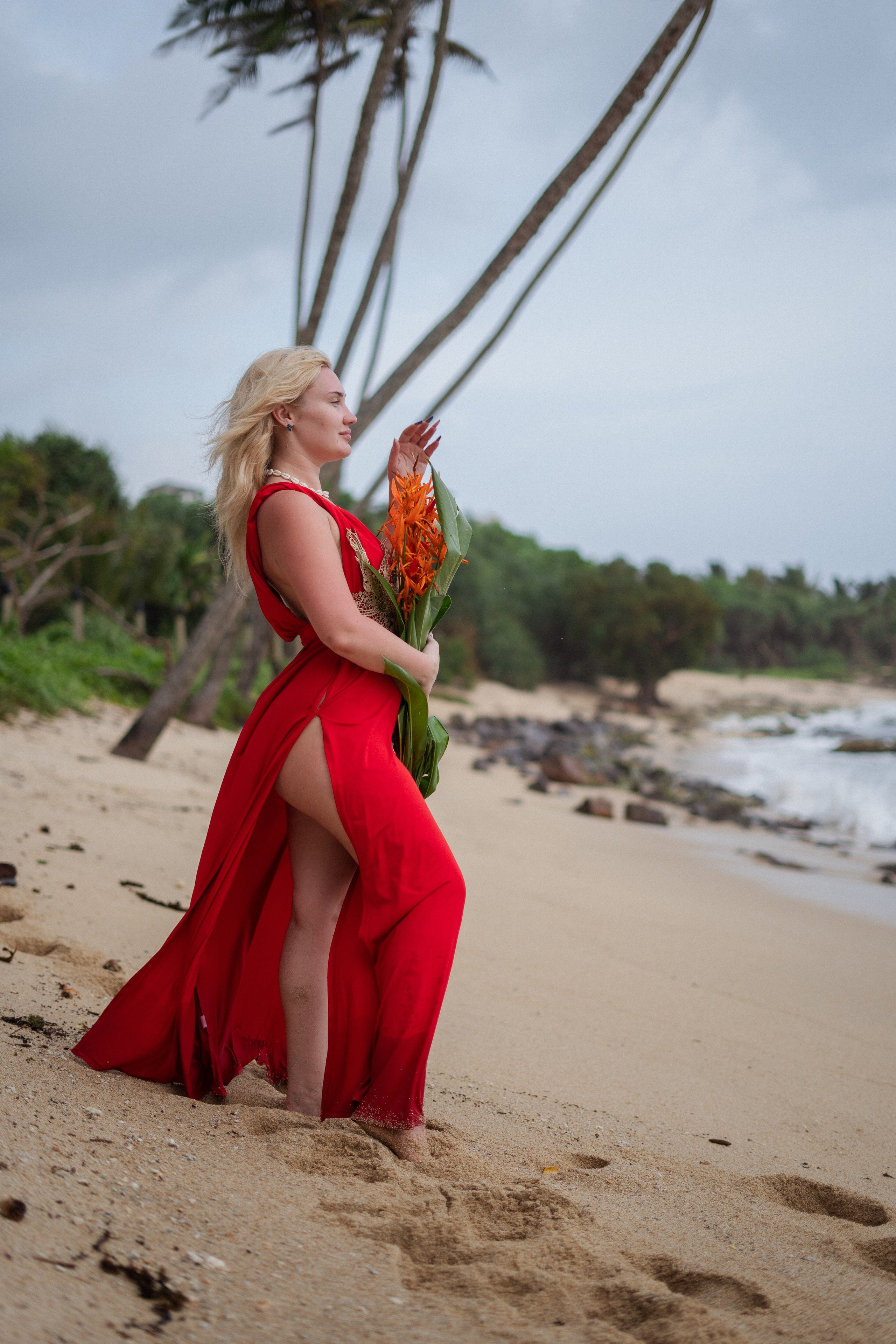 a blonde in a red dress with the ocean in the background