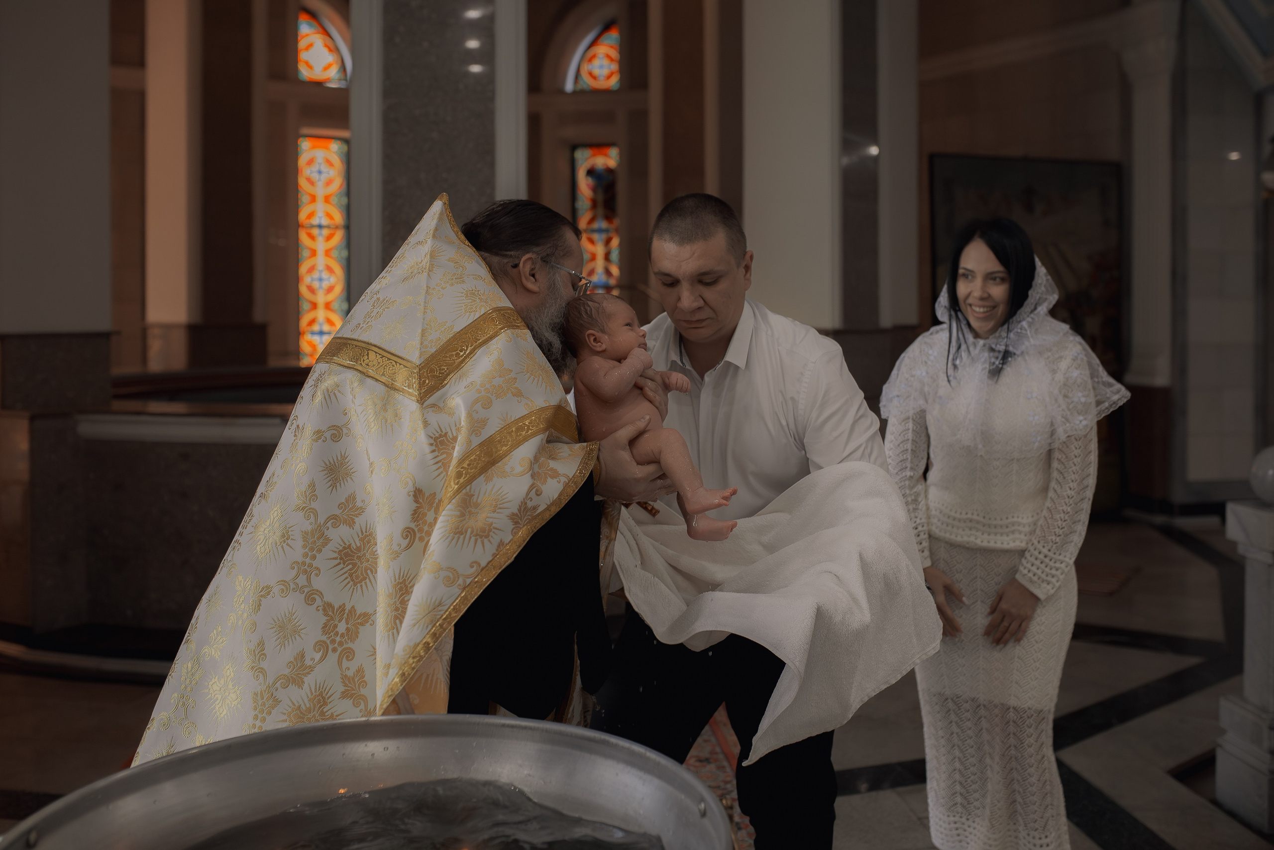 Крестный принимает ребенка из купели в Успенском соборе Ташкента