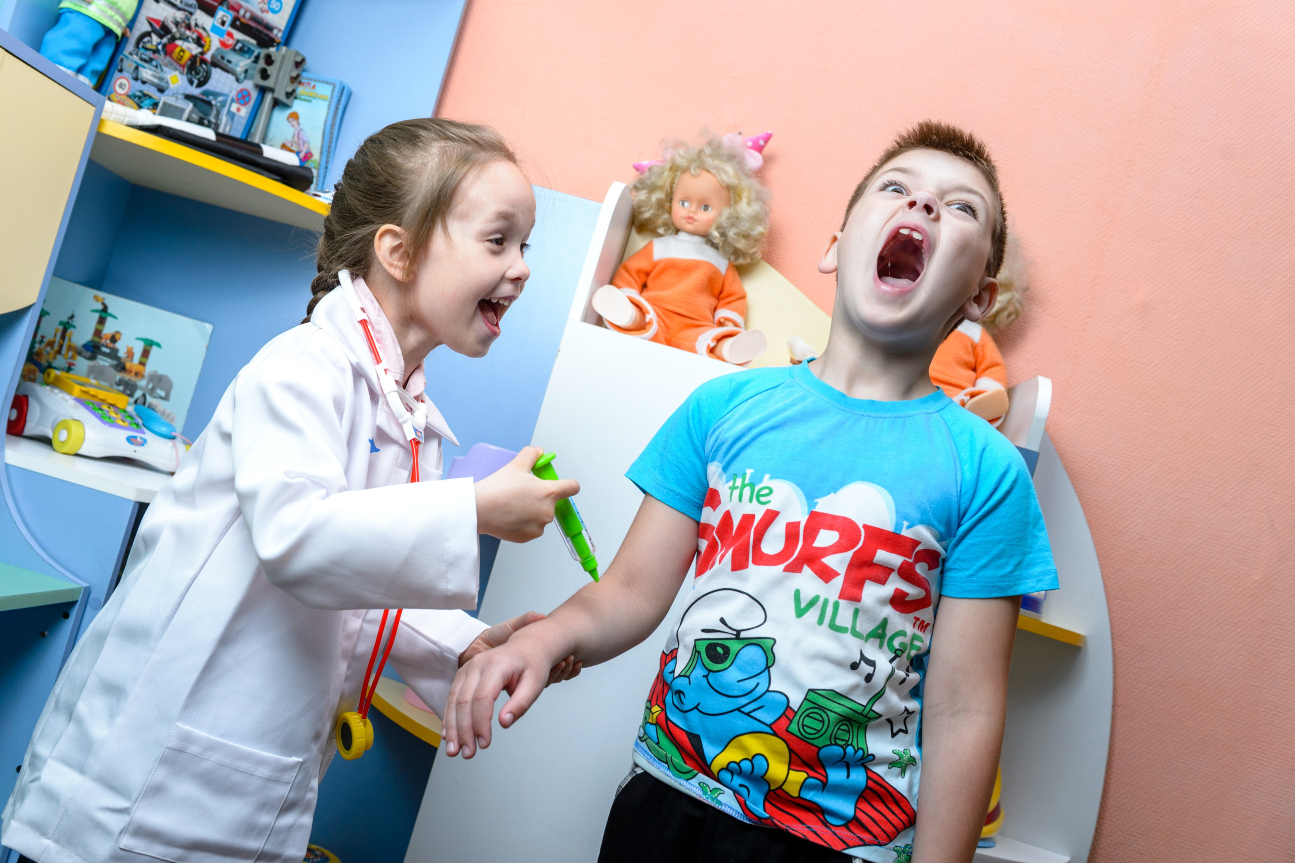 Девочка в костюме врача играет с мальчиком во врача и делает ему укол.