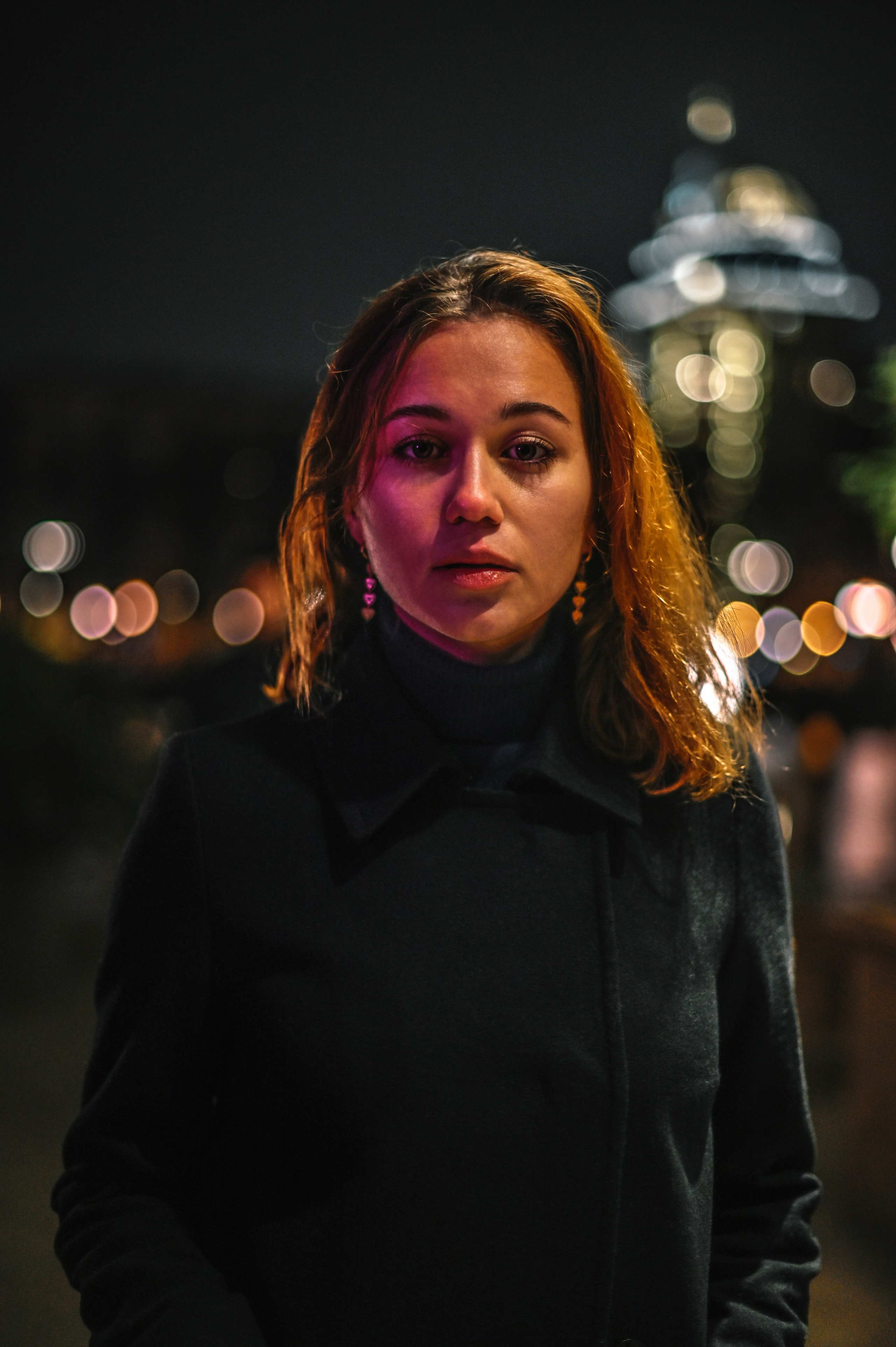 Ночной портрет стильной женщины с волнистыми волосами, снятый в Москве на фоне размытого городского фона с цветными огнями.