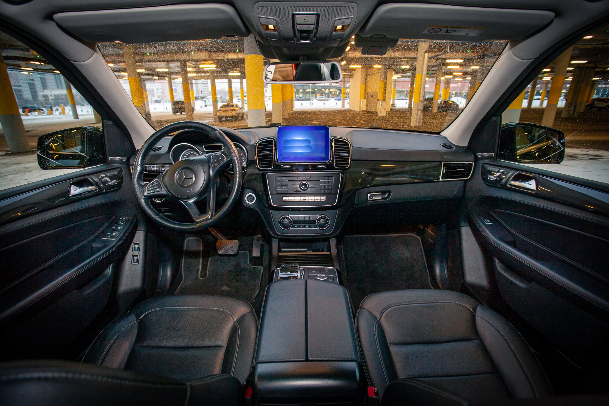 Широкий обзор интерьера Mercedes-Benz с кожаными сиденьями, рулевым колесом и центральной консолью. Современный дизайн и высокое качество отделки.