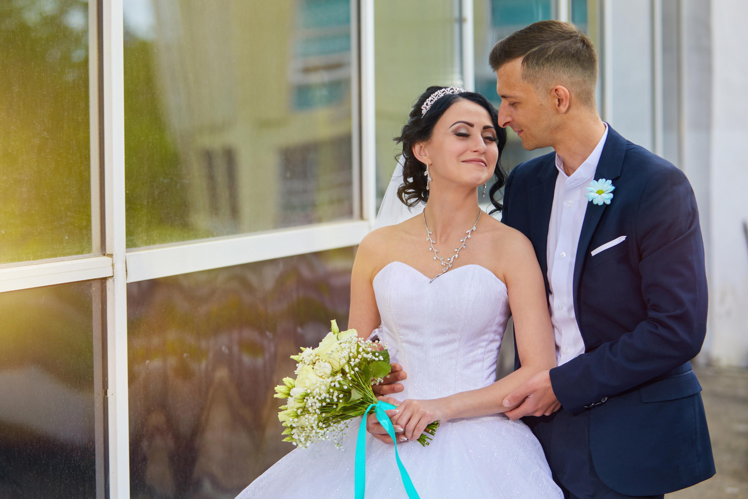 Жених и невеста целуются на фоне больших окон ЗАГСА