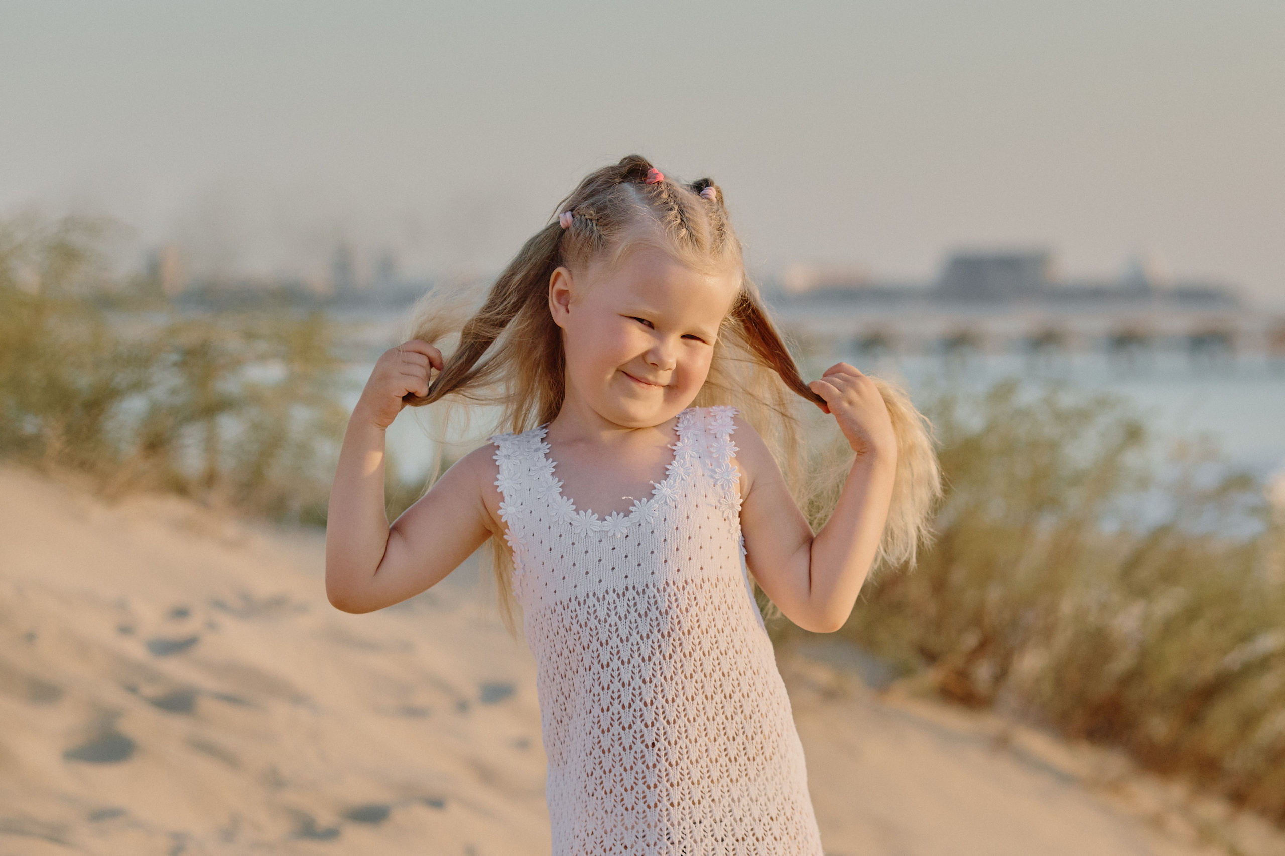 Девочка улыбается на камеру и держит себя за хвостики