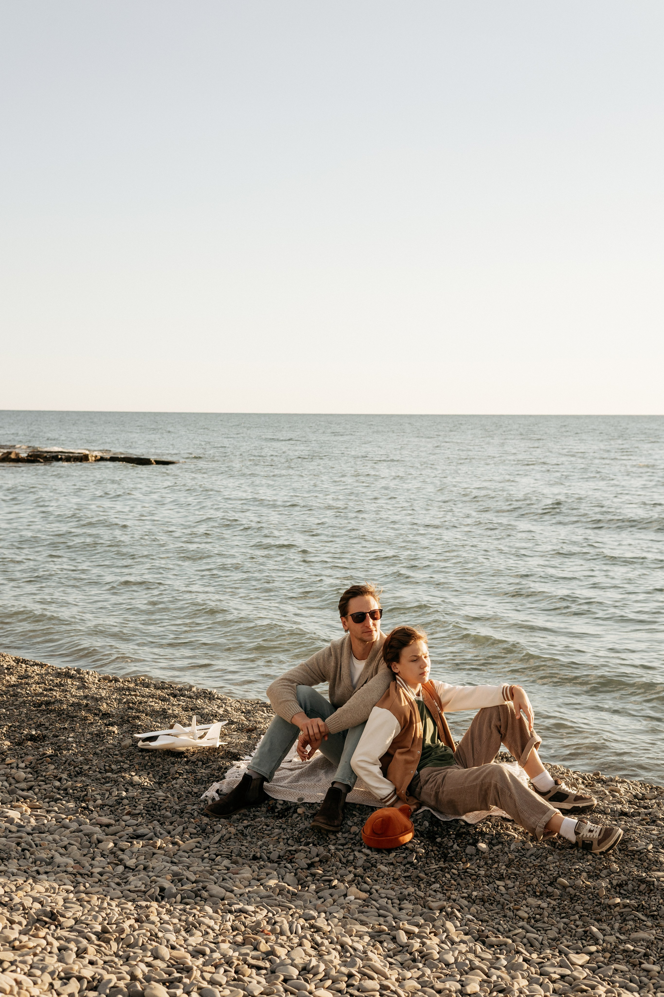 Папа с старшим сыном сидят на берегу черного моря и провожают закат