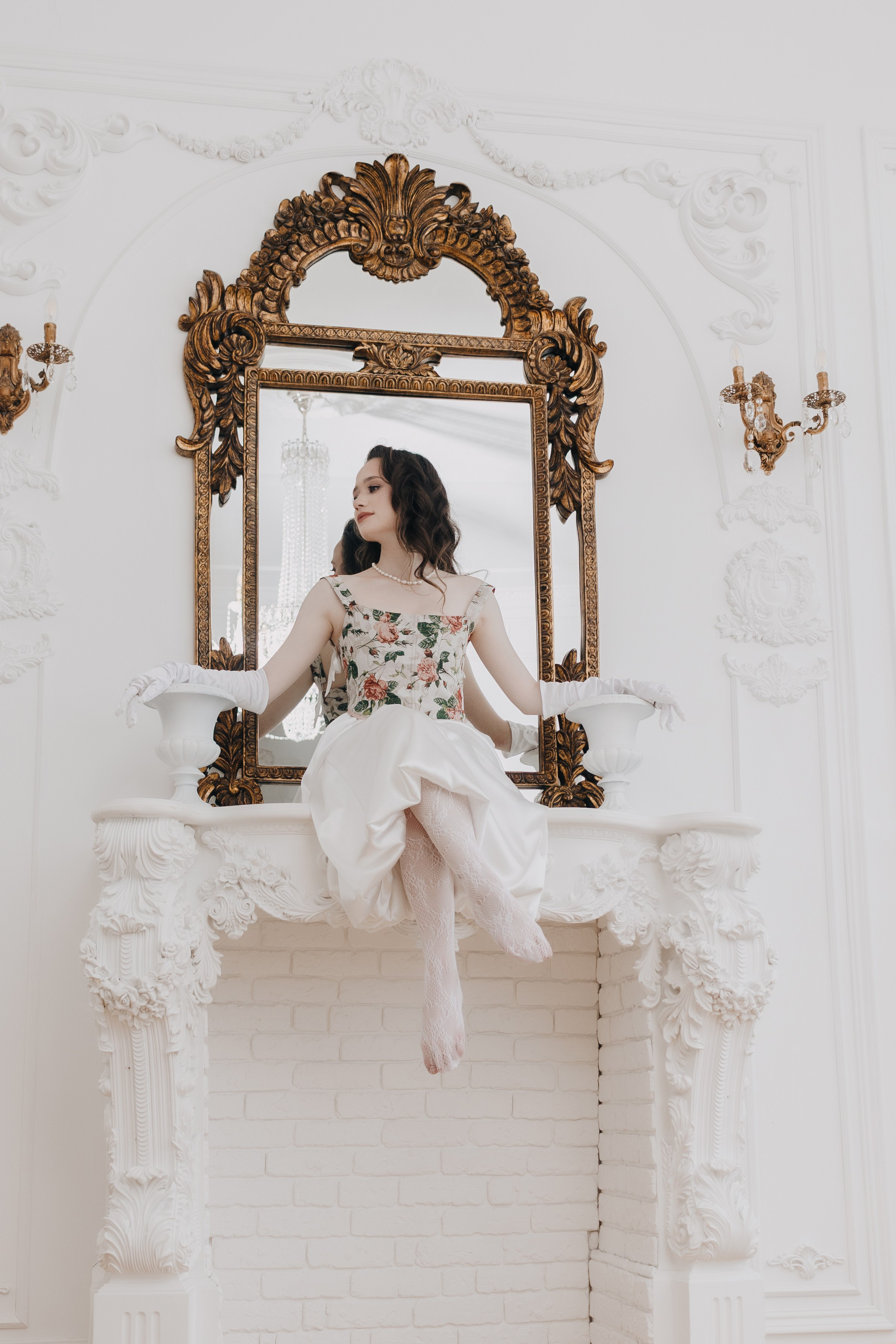 Александра Овечкина, Пенза: модель сидит на белом камине под золотым зеркалом, классический интерьер студии.